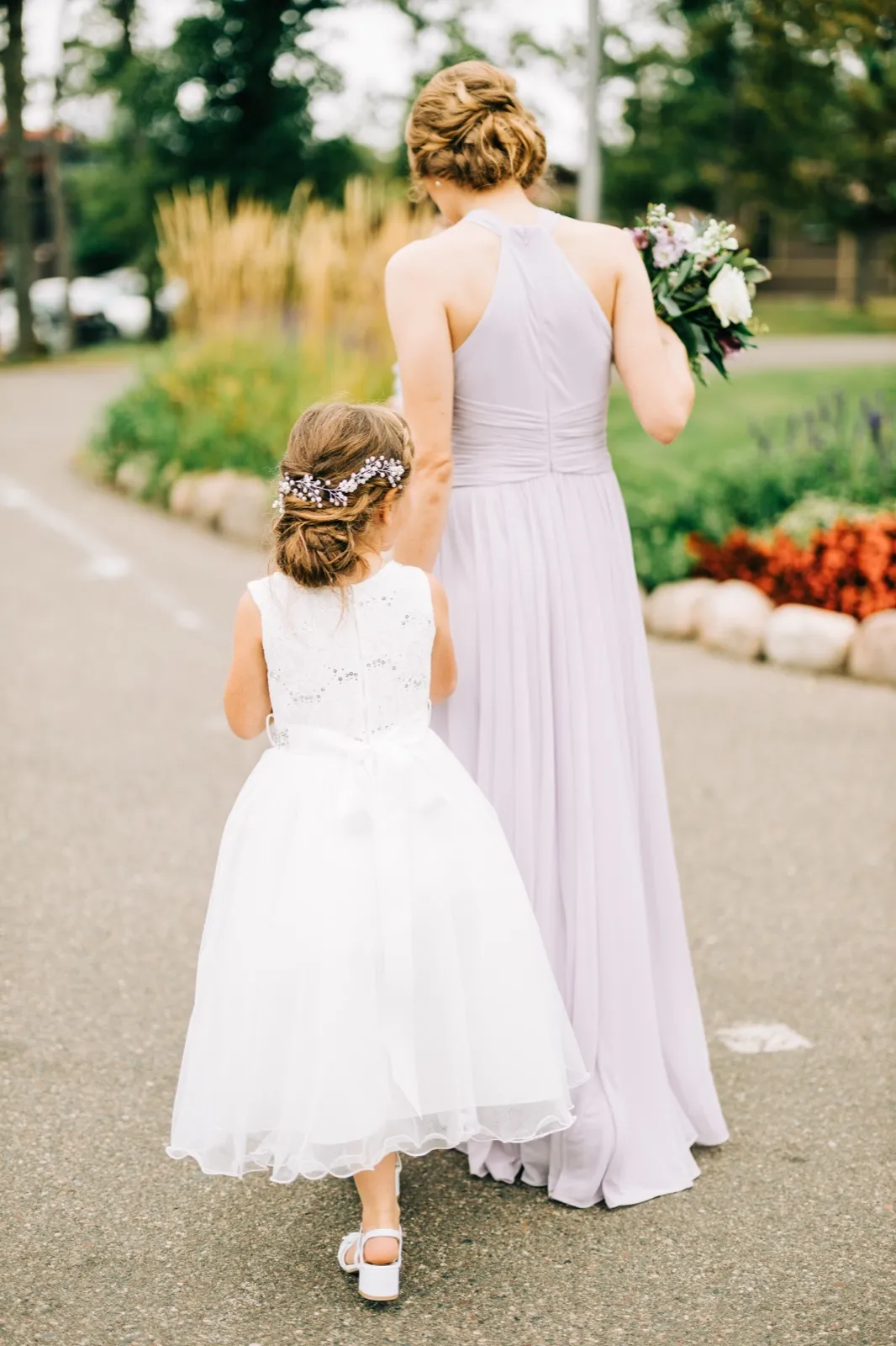 The flower girl holds hands with a bridesmaid in lavender as they walk away down a garden path at Madden's — Tim Larsen Photography, Brainerd Lakes MN