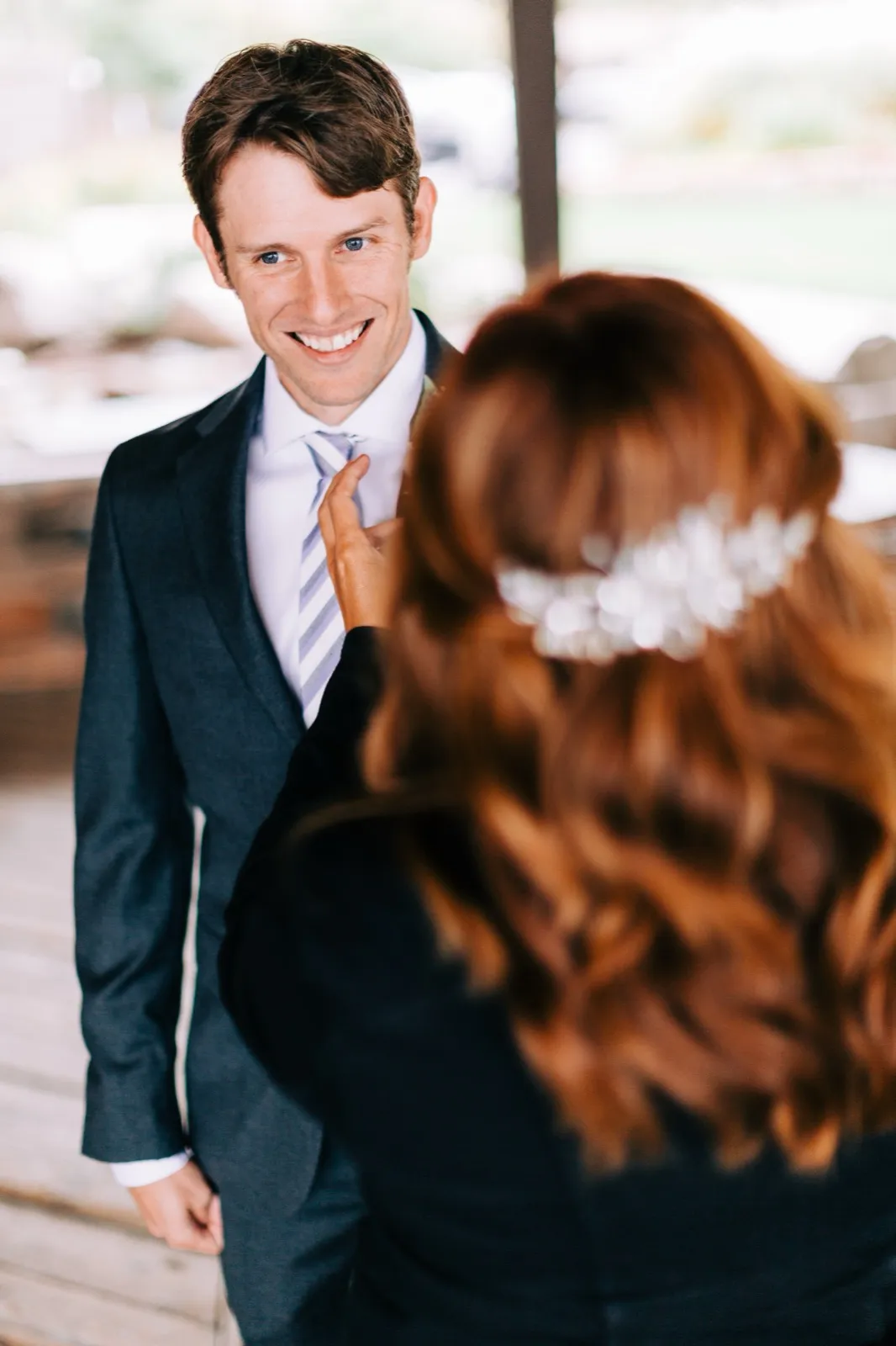 Brenden beams during the first look on a covered porch as Katie reaches toward his tie at Madden's on Gull Lake — Tim Larsen Photography, Brainerd Lakes MN