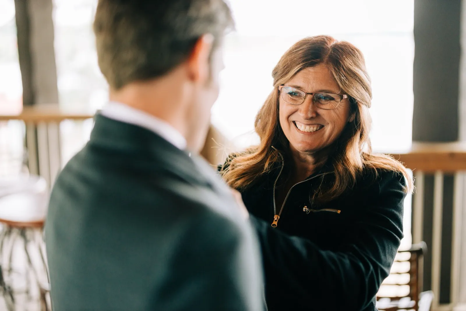 A woman in glasses laughs warmly while greeting Brenden on a covered porch — Tim Larsen Photography, Brainerd Lakes MN