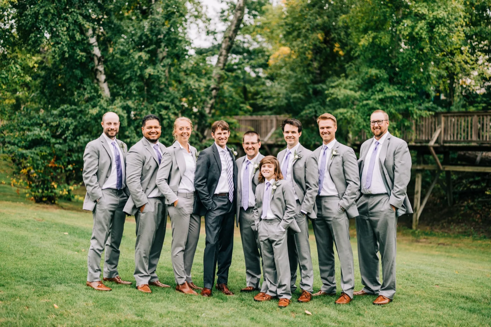 Brenden stands with his groomsmen, a groomswoman, and a young attendant in gray suits and lavender ties on a lawn at Madden's — Tim Larsen Photography, Brainerd Lakes MN