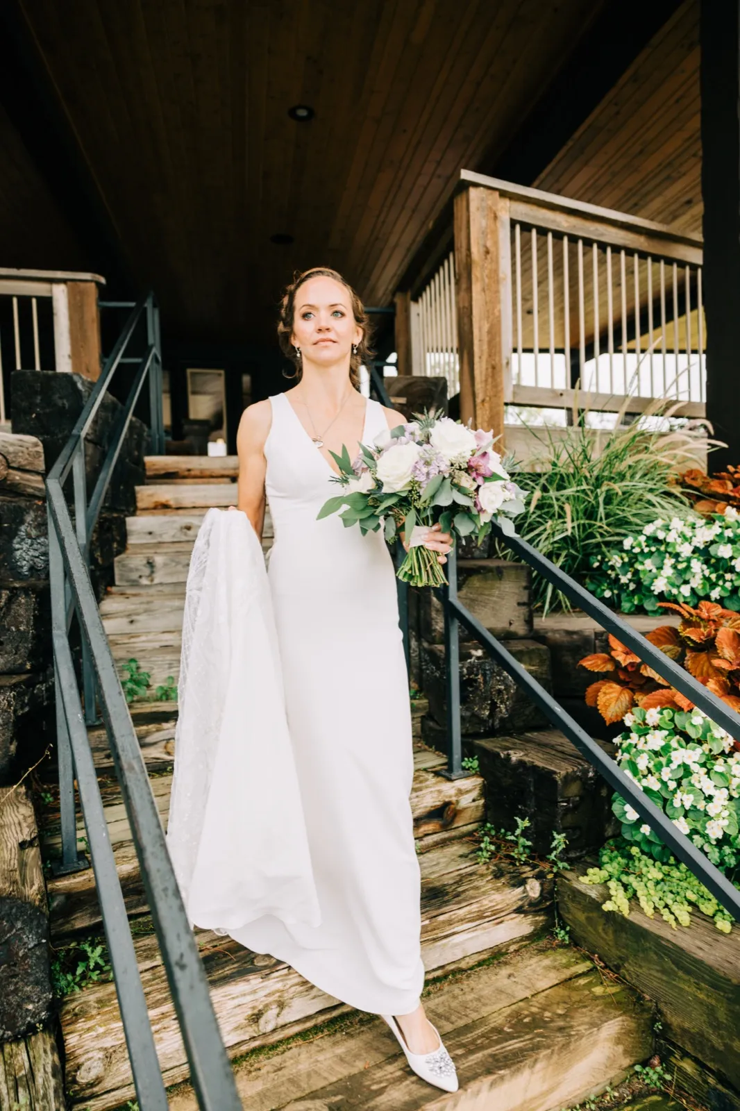 Katie comes down the wooden stairs beneath the lodge deck with her bouquet and train in hand on the way to her first look — Tim Larsen Photography, Brainerd Lakes MN