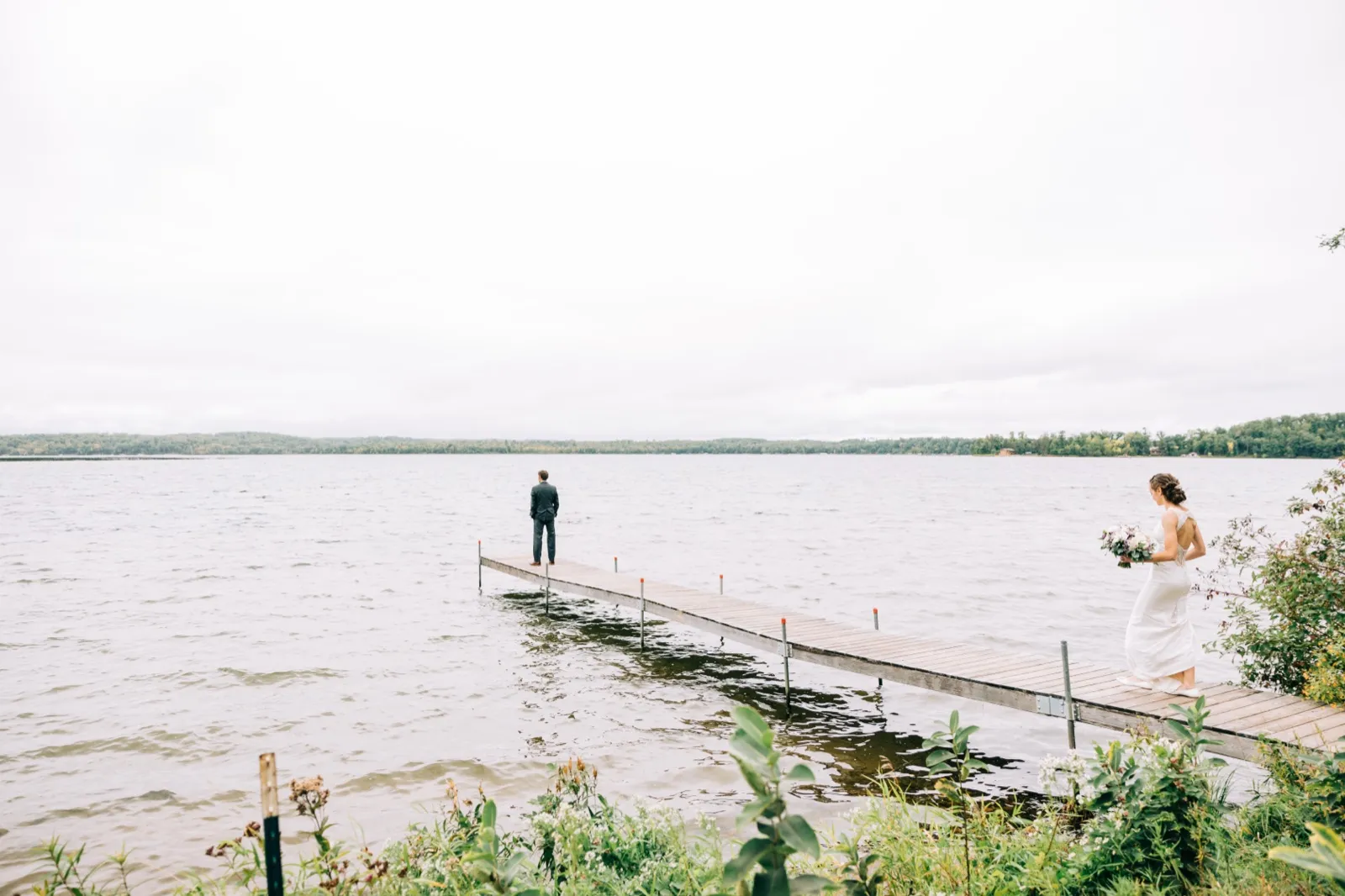 Katie walks out the long dock toward Brenden, who stands at the end facing Gull Lake, for their first look at Madden's — Tim Larsen Photography, Brainerd Lakes MN
