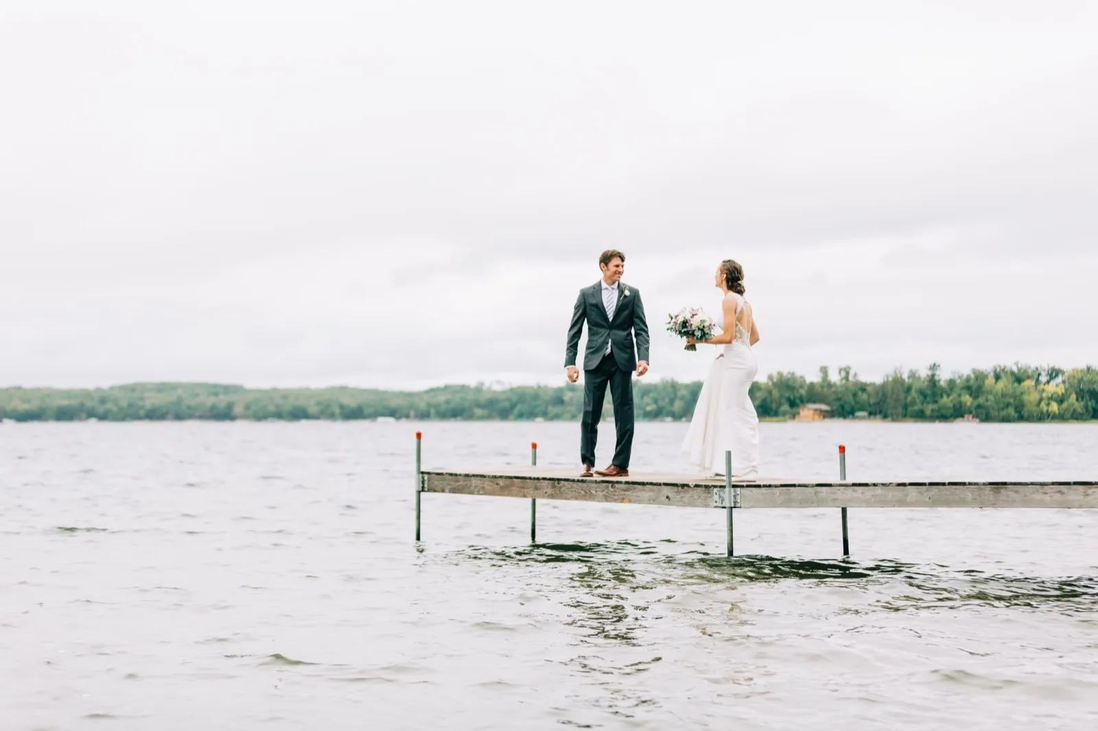Katie and Brenden stand facing each other on a long dock reaching into Gull Lake under a soft overcast sky — Tim Larsen Photography, Brainerd Lakes MN
