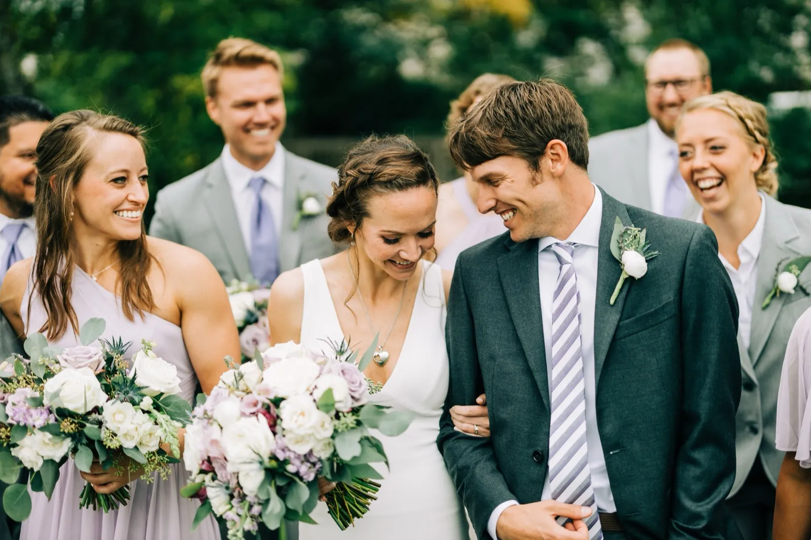 Katie and Brenden share a private laugh as their bridesmaids and groomsmen laugh around them, bouquets in the foreground — Tim Larsen Photography, Brainerd Lakes MN