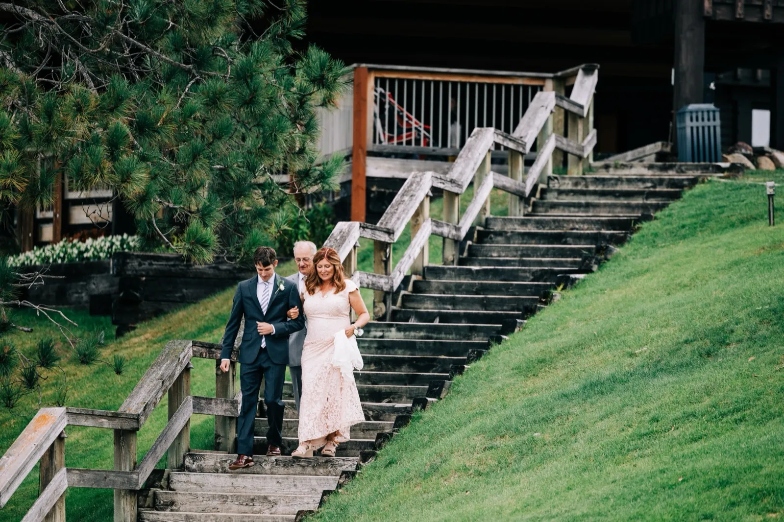 Katie walks down a long wooden lakeside staircase on her father's arm toward the ceremony, the resort's tiered decks behind — Tim Larsen Photography, Brainerd Lakes MN