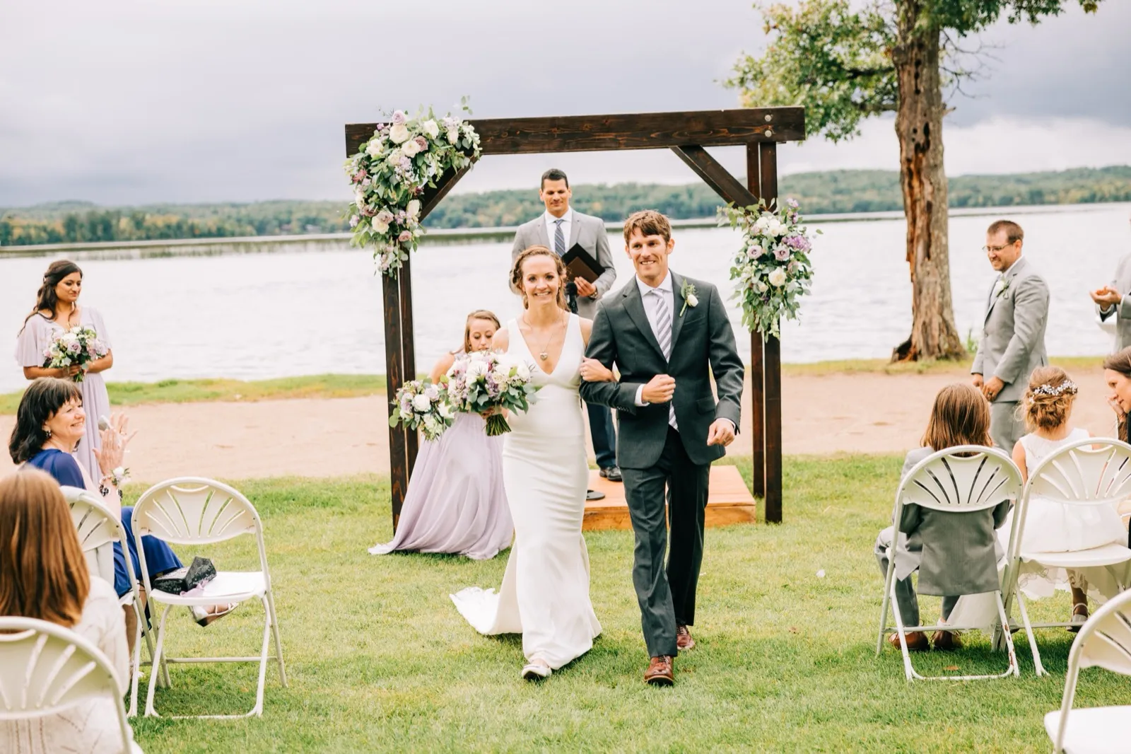 Katie and Brenden walk back down the aisle smiling beneath the floral arch, Gull Lake stretching behind them — Tim Larsen Photography, Brainerd Lakes MN