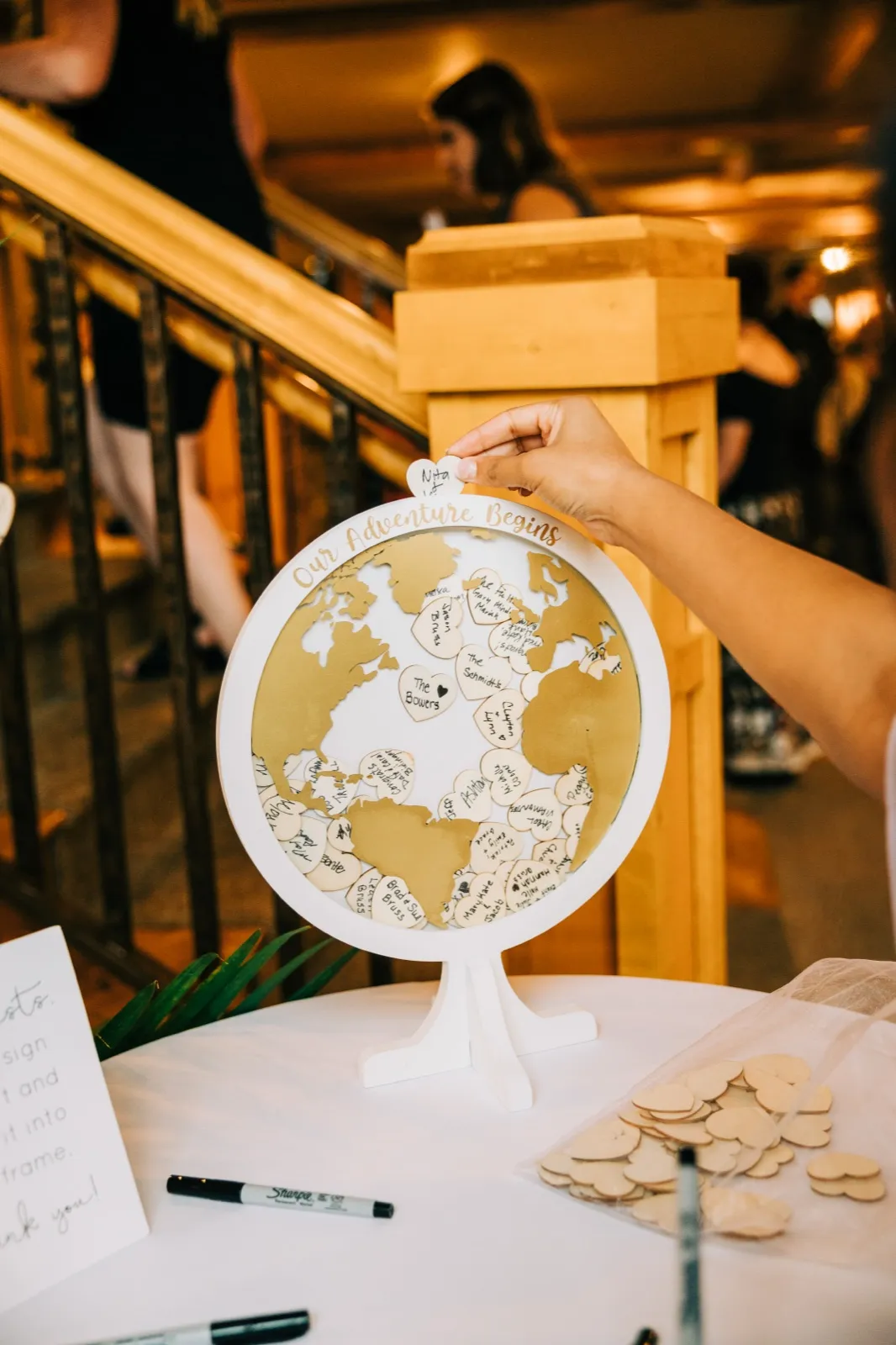 A guest drops a signed wooden heart into a globe-shaped guest book frame on a reception table — Tim Larsen Photography, Brainerd Lakes MN