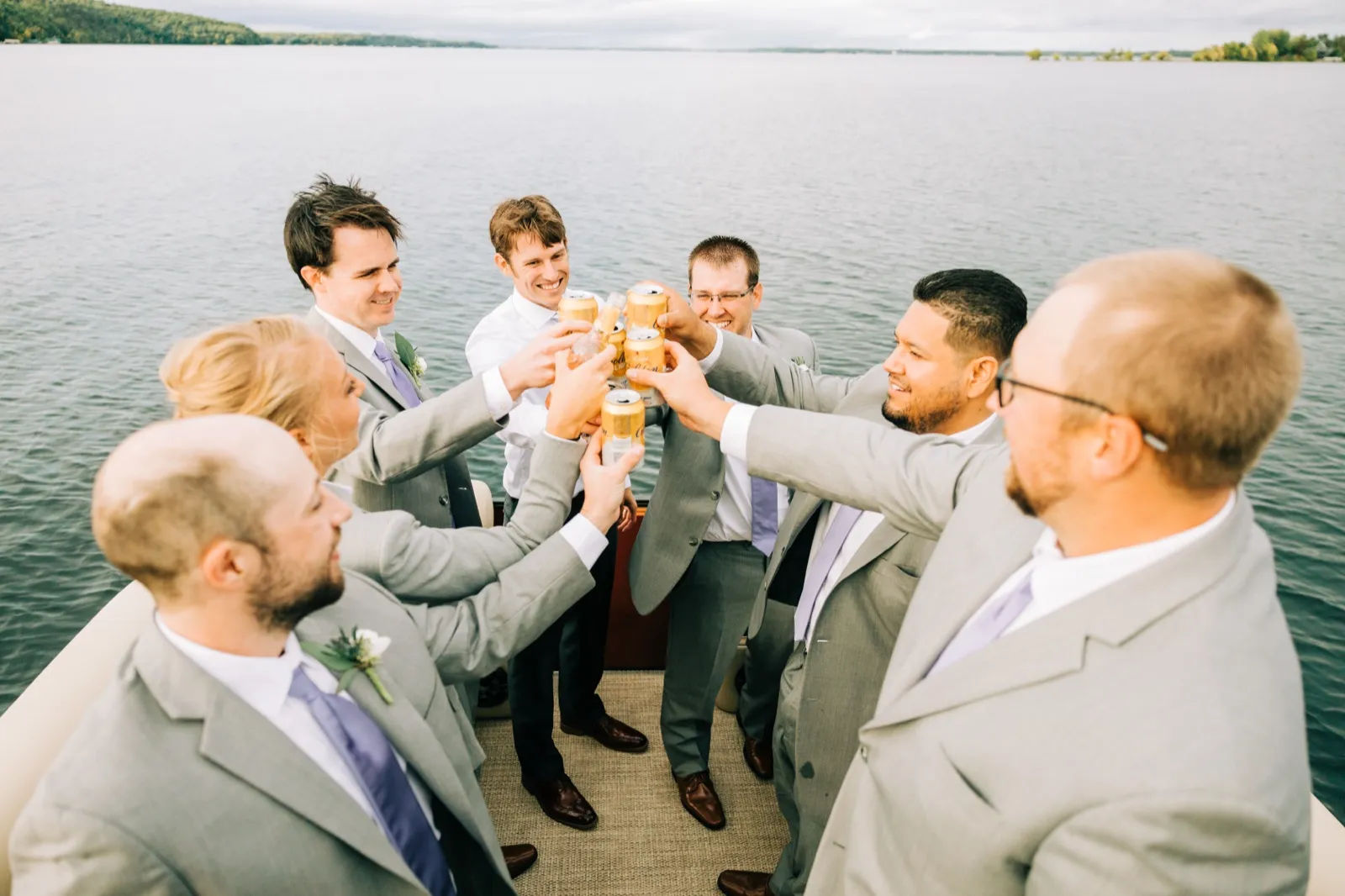 The groomsmen and groomswoman knock beer cans together in a huddle aboard a pontoon on Gull Lake — Tim Larsen Photography, Brainerd Lakes MN