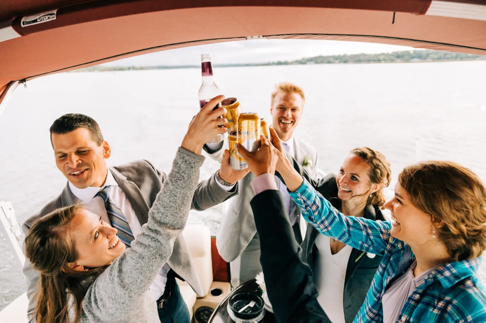 Katie and friends raise beer cans and a bottle in a toast under the canopy of a pontoon on Gull Lake — Tim Larsen Photography, Brainerd Lakes MN