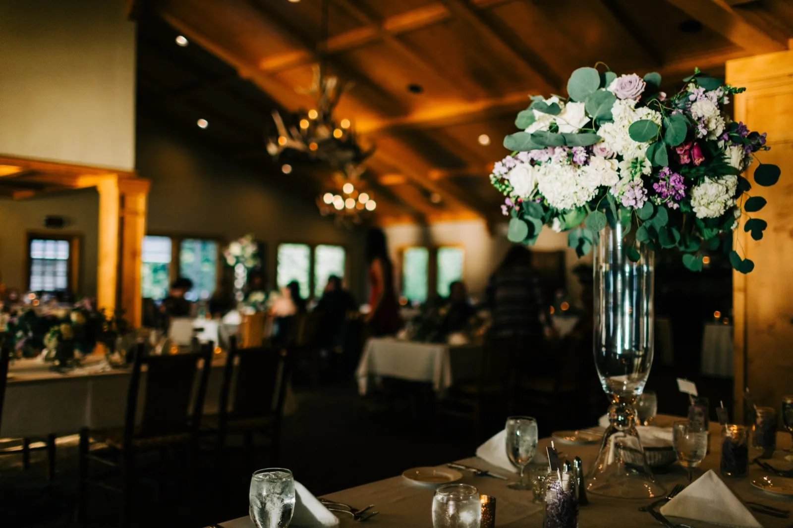A purple-and-white floral centerpiece on a set table in the wood-beamed reception ballroom with antler chandeliers at Madden's — Tim Larsen Photography, Brainerd Lakes MN