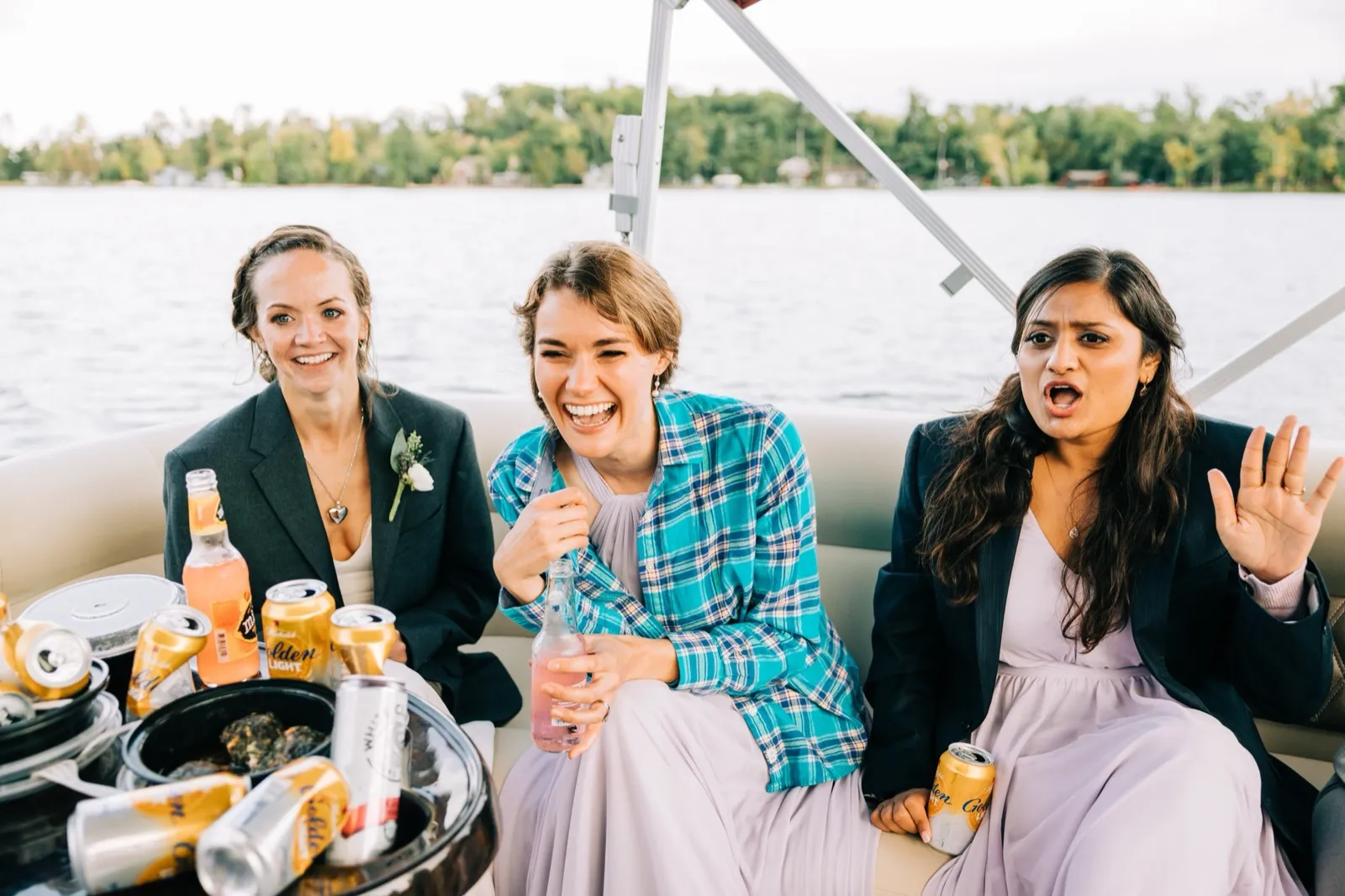 Katie laughs between two bridesmaids on a pontoon boat, drinks on a cooler in the foreground and Gull Lake behind — Tim Larsen Photography, Brainerd Lakes MN