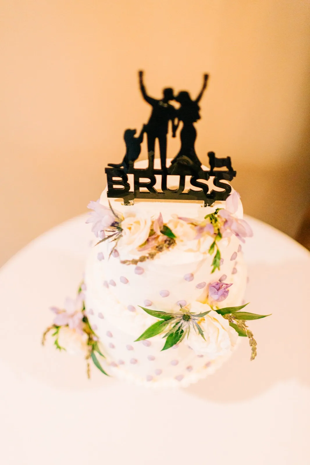 A two-tier white wedding cake dotted in lavender and trimmed with pastel flowers, topped with a black cutout cake topper — Tim Larsen Photography, Brainerd Lakes MN