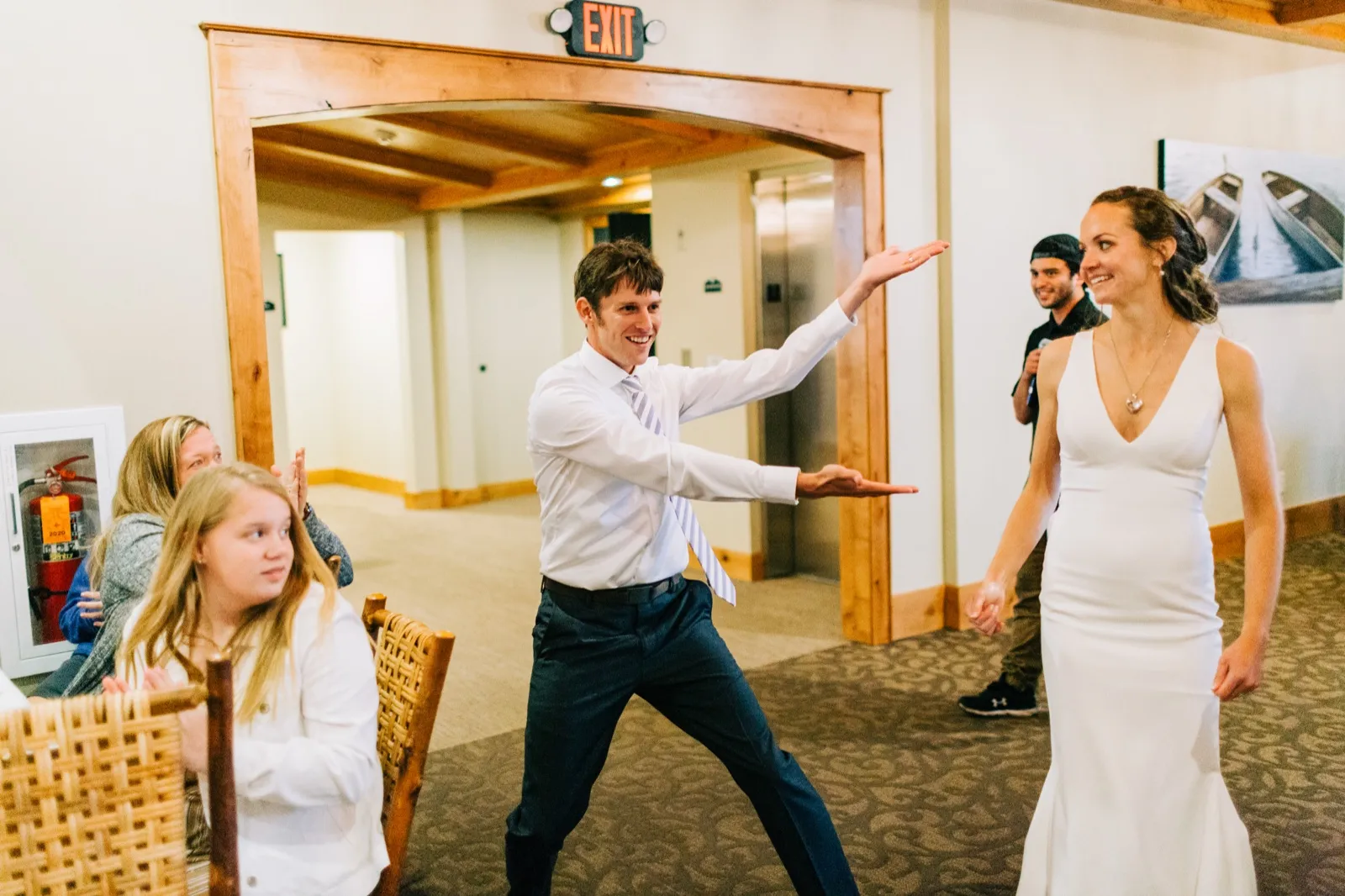 Brenden throws his arms wide in a ta-da pose as Katie walks into the reception smiling at Madden's on Gull Lake — Tim Larsen Photography, Brainerd Lakes MN