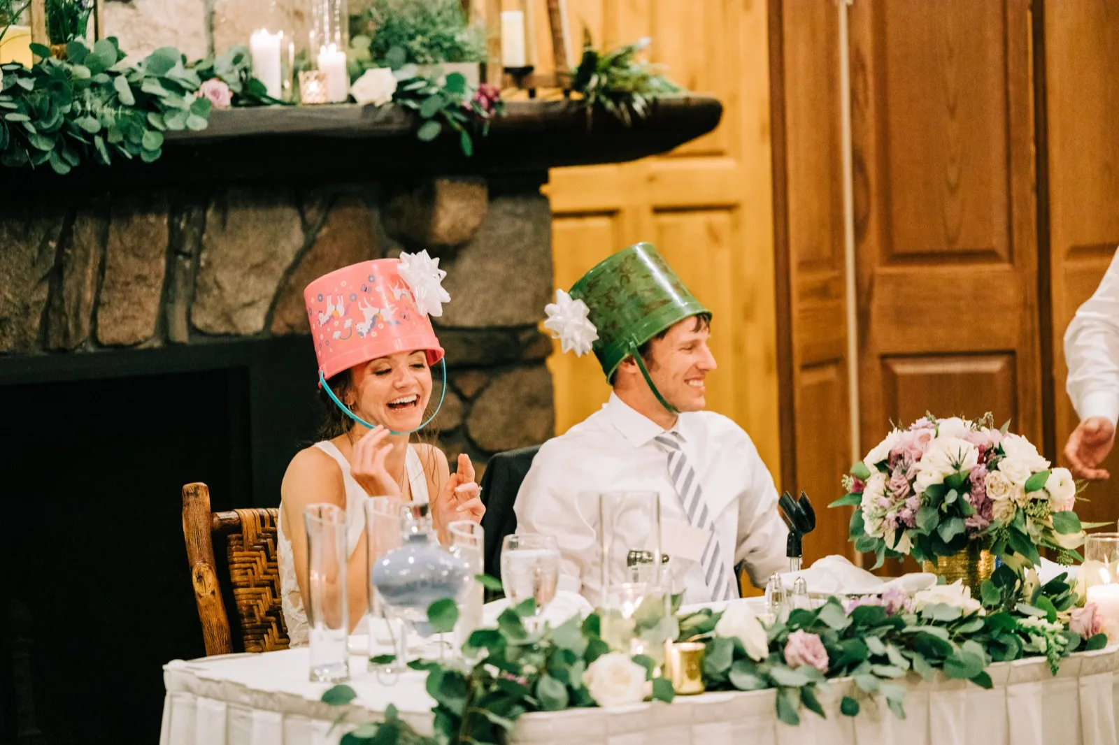 Katie and Brenden laugh at the head table wearing bow-topped buckets as hats — Tim Larsen Photography, Brainerd Lakes MN