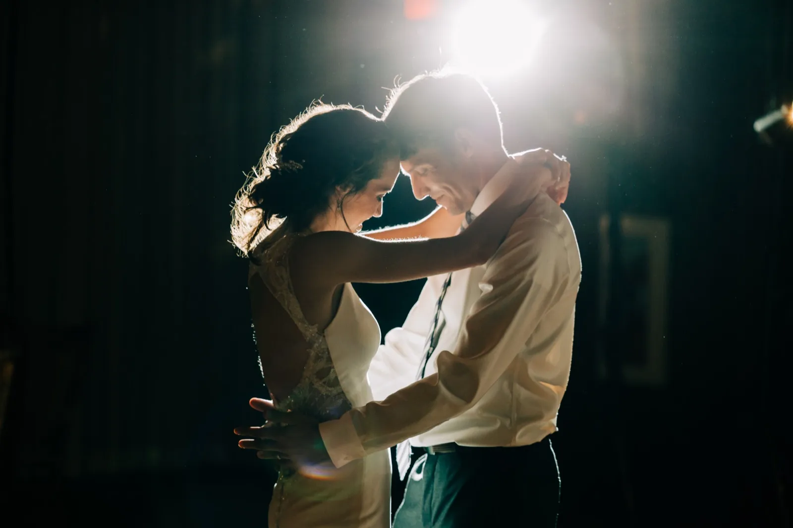 Katie and Brenden press their foreheads together during their first dance, rim-lit by a single light in the dark reception hall at Madden's on Gull Lake — Tim Larsen Photography, Brainerd Lakes MN