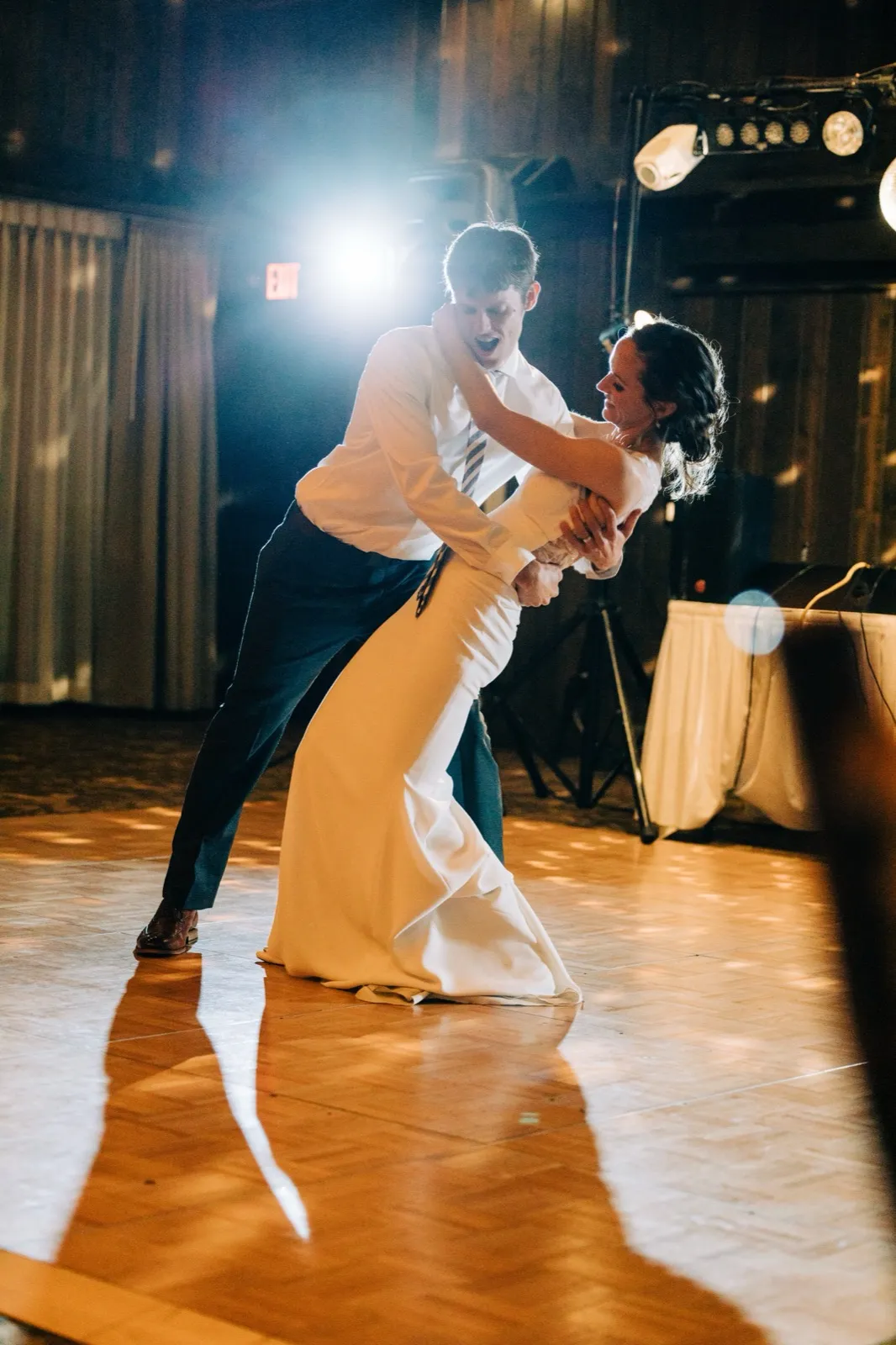 Brenden dips Katie on the parquet dance floor as a stage light flares behind them, casting their shadow across the floor — Tim Larsen Photography, Brainerd Lakes MN