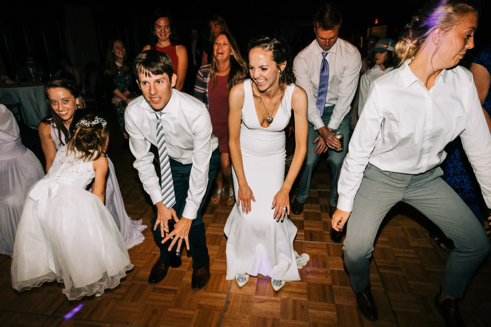Katie and Brenden crouch low mid-dance with the flower girl and guests on the parquet dance floor — Tim Larsen Photography, Brainerd Lakes MN