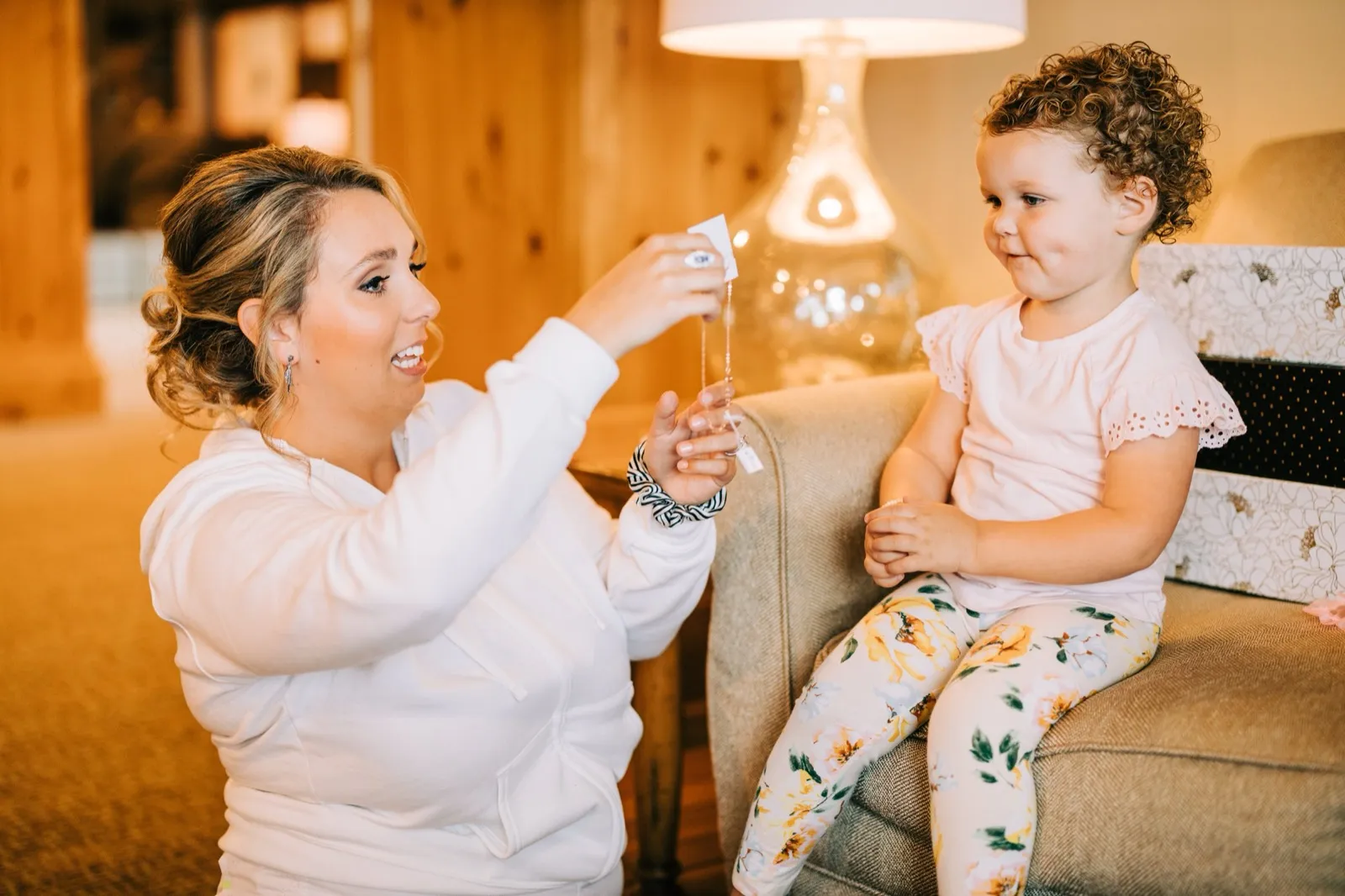 Hailee shows her necklace to a small flower girl on the couch as she finishes getting ready — Tim Larsen Photography, Brainerd Lakes MN