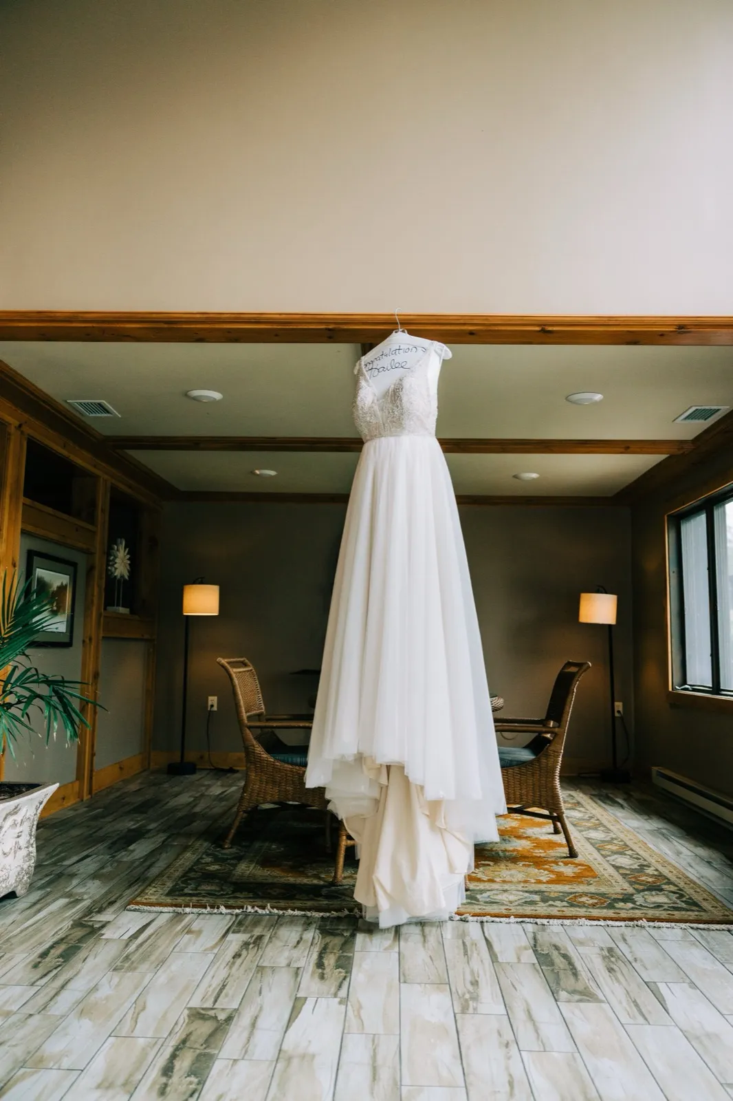 Hailee's gown hangs from a personalized hanger between two floor lamps in the wood-trimmed getting-ready room — Tim Larsen Photography, Brainerd Lakes MN