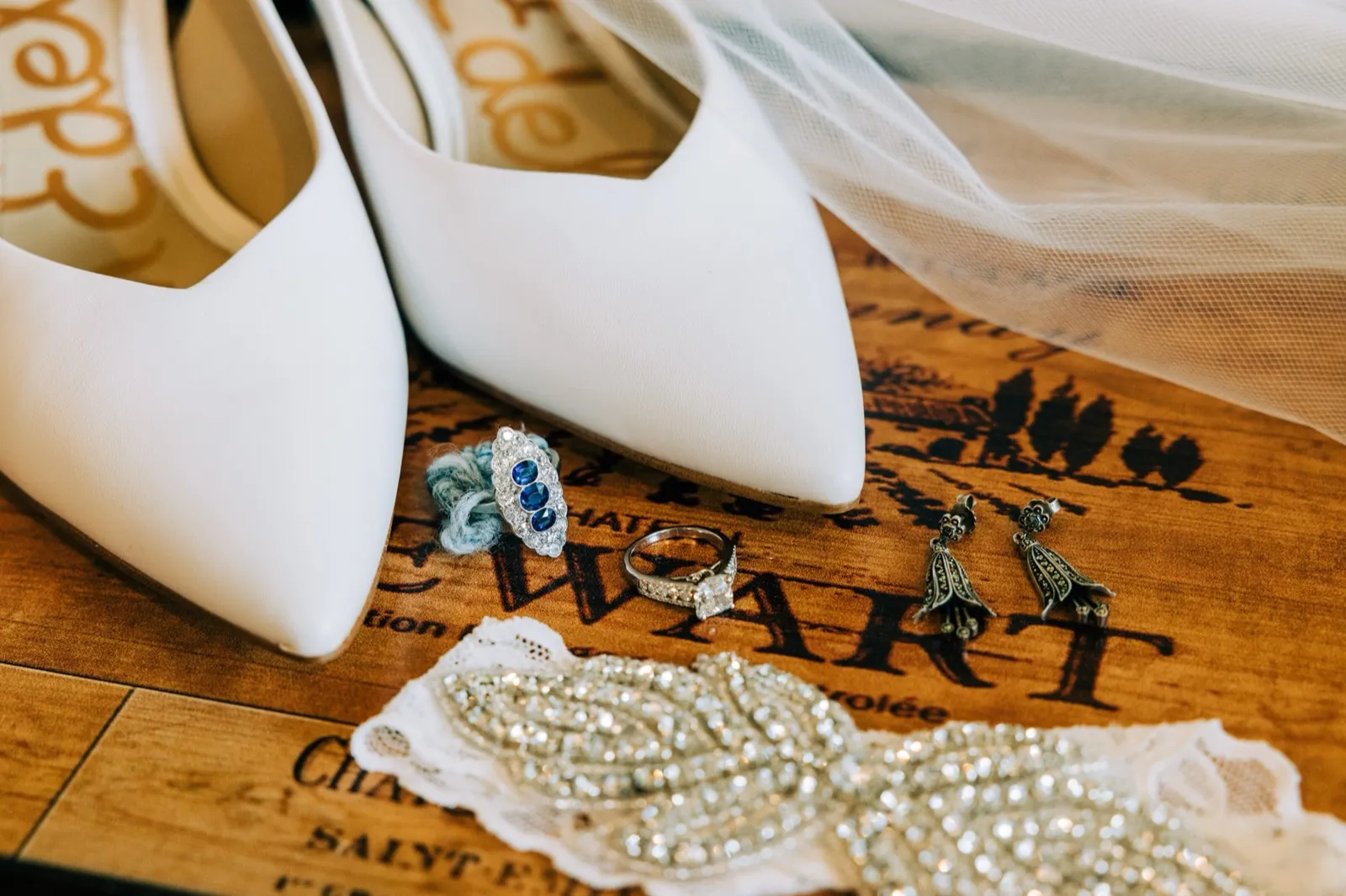 Hailee's white heels, sapphire-and-diamond rings, marcasite drop earrings, and beaded garter arranged on a wine crate with the veil — Tim Larsen Photography, Brainerd Lakes MN