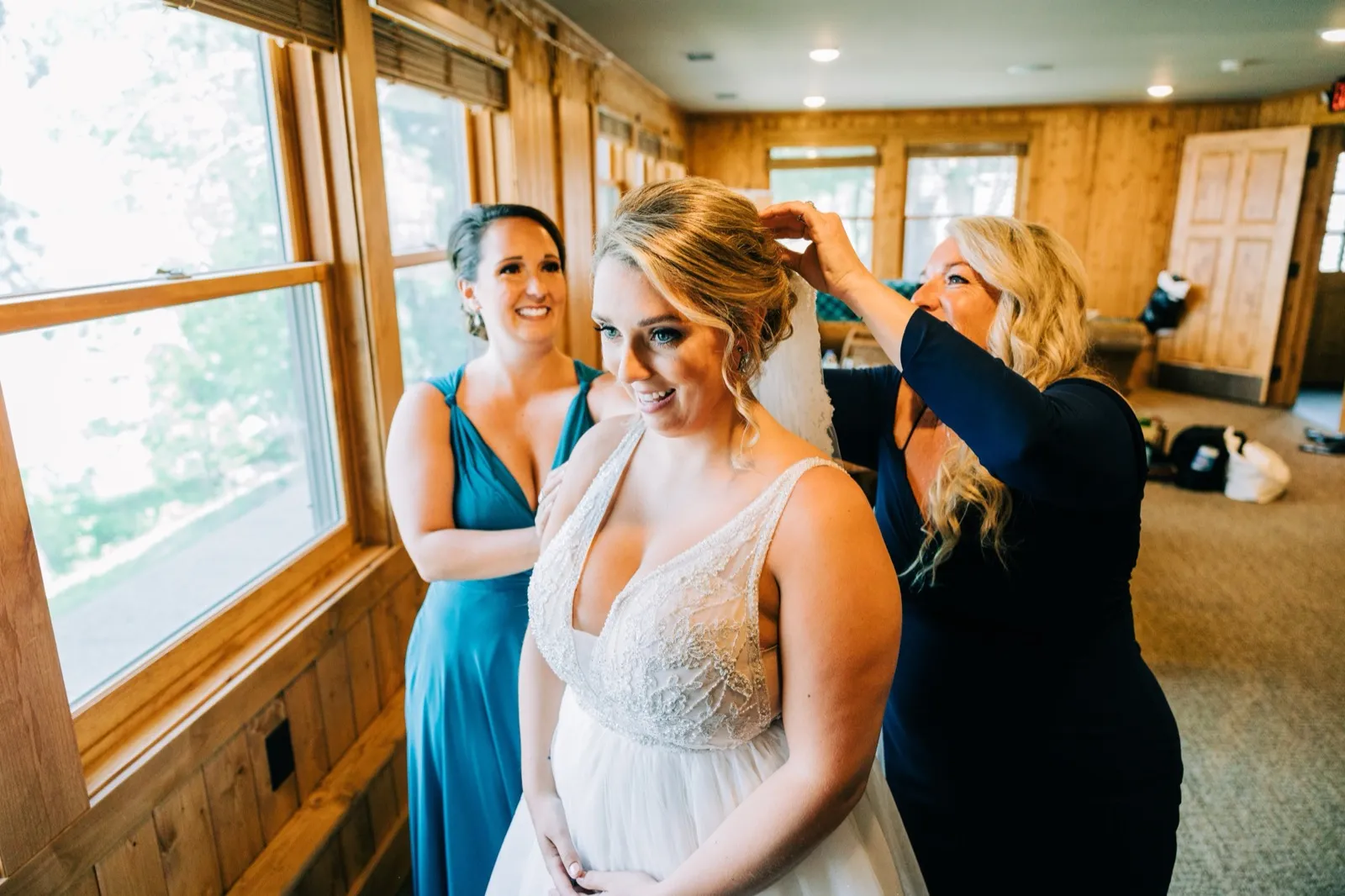 Hailee's mother fastens her veil as a bridesmaid in teal looks on in the window-lit bridal suite at Madden's — Tim Larsen Photography, Brainerd Lakes MN