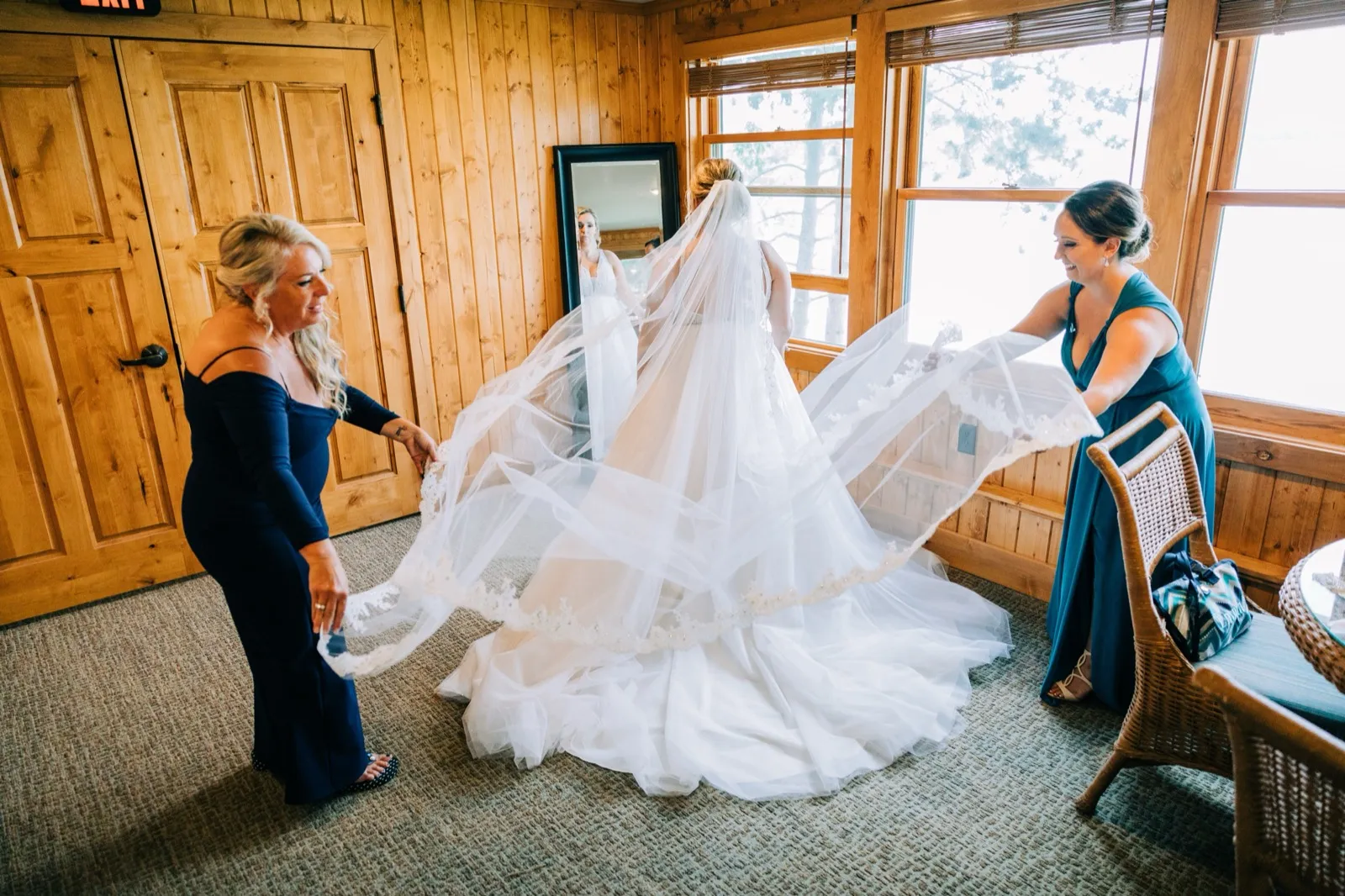 Two women fan Hailee's long veil and ballgown train across the floor of the wood-paneled bridal suite — Tim Larsen Photography, Brainerd Lakes MN