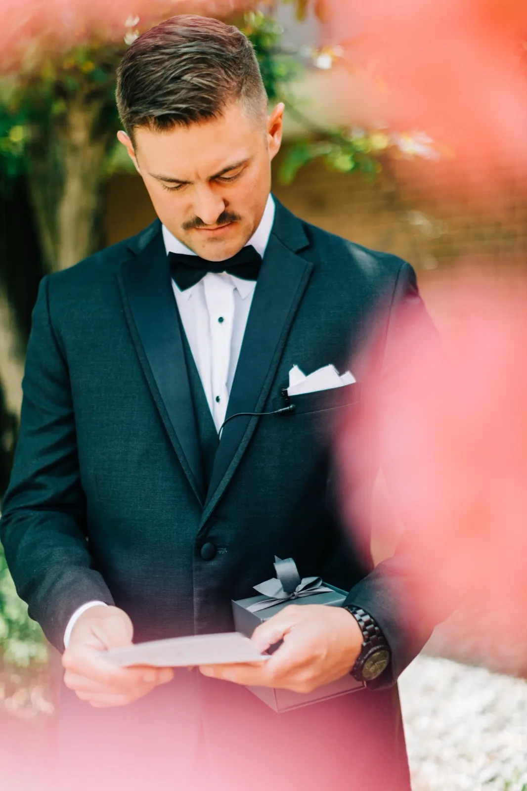 Jonathon reads a handwritten note and holds a ribbon-tied gift box outdoors, framed by soft pink foliage — Tim Larsen Photography, Brainerd Lakes MN