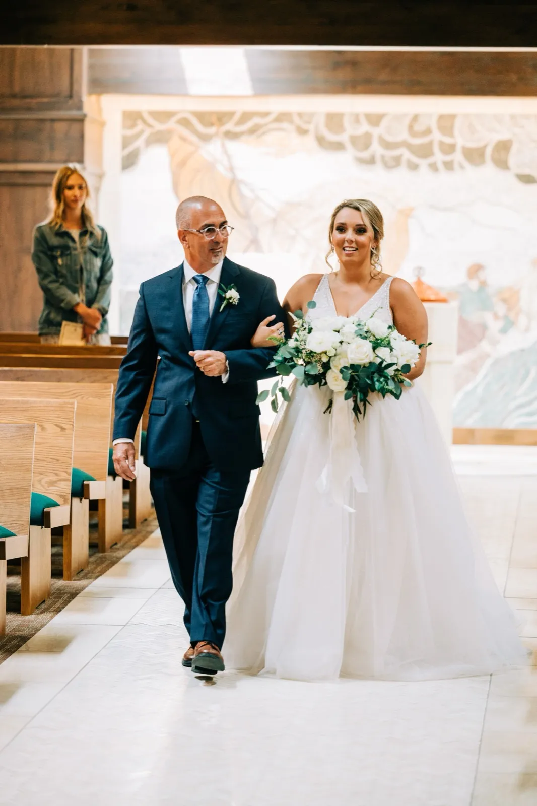 Hailee beams walking down the aisle on her father's arm at St. Andrew's Catholic Church, holding a white-and-green bouquet — Tim Larsen Photography, Brainerd Lakes MN