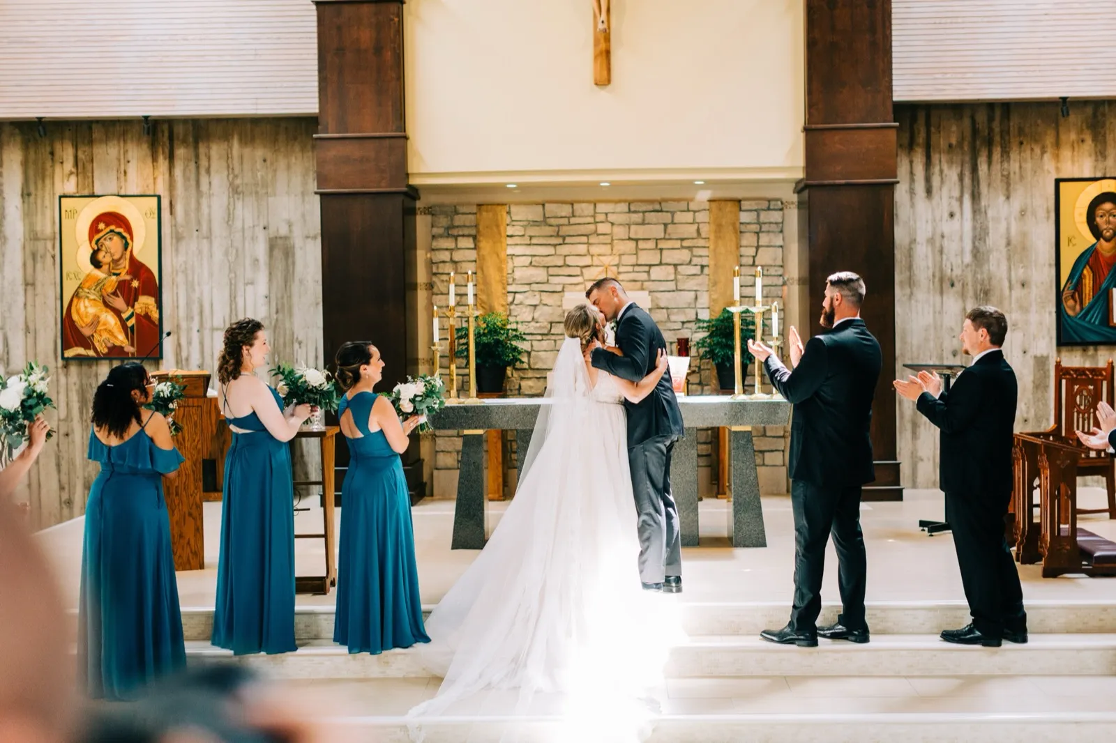 Hailee and Jonathon share their first kiss at the stone altar of St. Andrew's Catholic Church in Brainerd as their bridal party applauds — Tim Larsen Photography, Brainerd Lakes MN