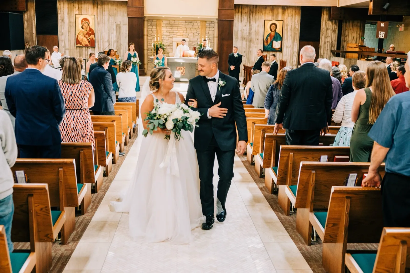 Hailee and Jonathon smile at each other walking back up the church aisle, just married — Tim Larsen Photography, Brainerd Lakes MN