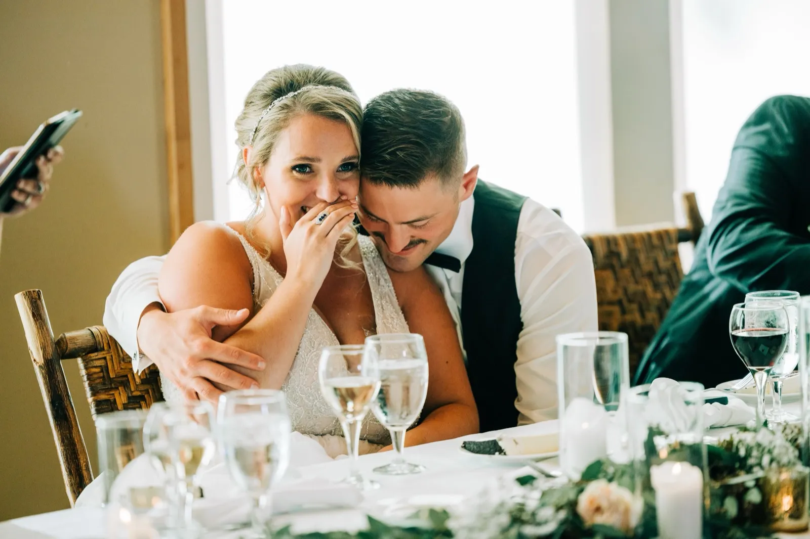 Hailee laughs behind her hand as Jonathon leans into her shoulder during toasts at the head table — Tim Larsen Photography, Brainerd Lakes MN