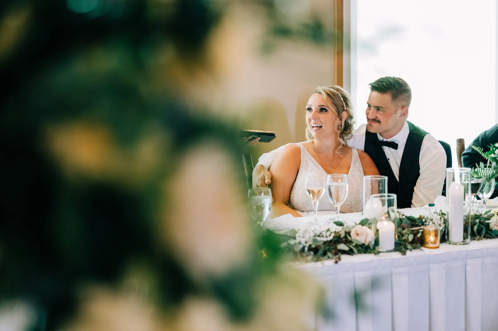 Hailee and Jonathon react to a toast at the head table, framed by soft centerpiece florals — Tim Larsen Photography, Brainerd Lakes MN