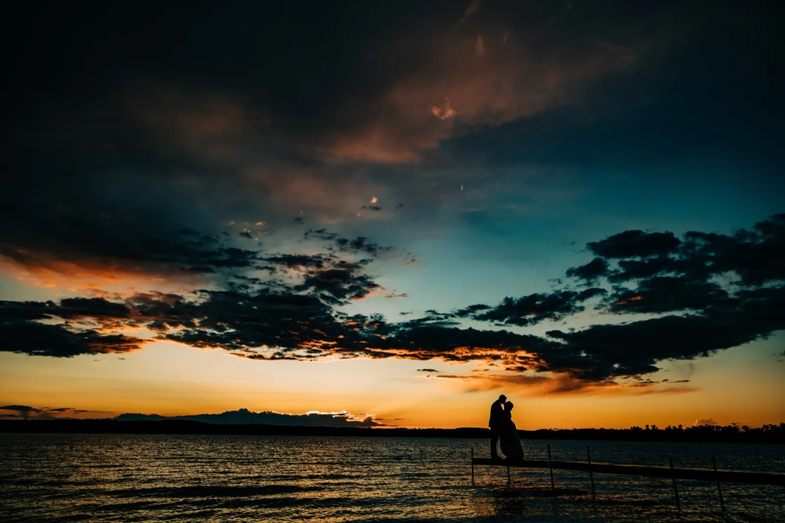 Hailee and Jonathon kiss in silhouette at the end of a long dock on Gull Lake beneath a teal-and-orange sunset — Tim Larsen Photography, Brainerd Lakes MN