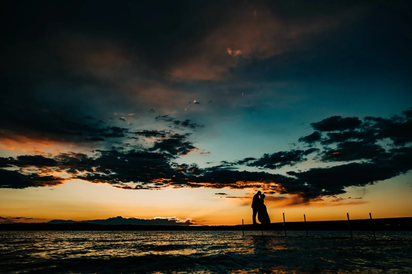 Hailee and Jonathon embrace in silhouette at the end of a dock on Gull Lake beneath an orange-and-teal sunset — Tim Larsen Photography, Brainerd Lakes MN