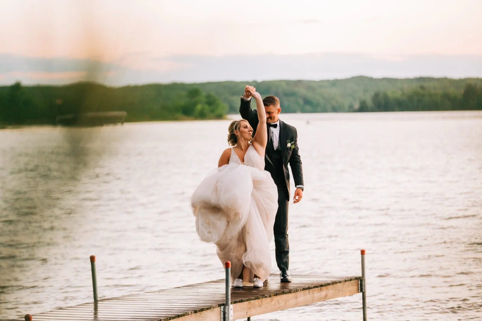 Jonathon twirls Hailee on a wooden dock at sunset, her tulle gown swirling above the still water of Gull Lake — Tim Larsen Photography, Brainerd Lakes MN