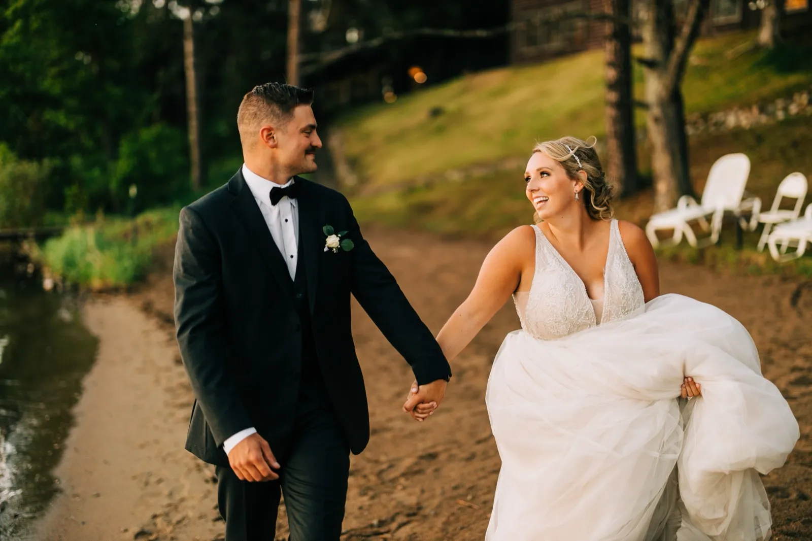 Hailee laughs back at Jonathon as they walk hand in hand along the sandy lakeshore at golden hour at Madden's — Tim Larsen Photography, Brainerd Lakes MN