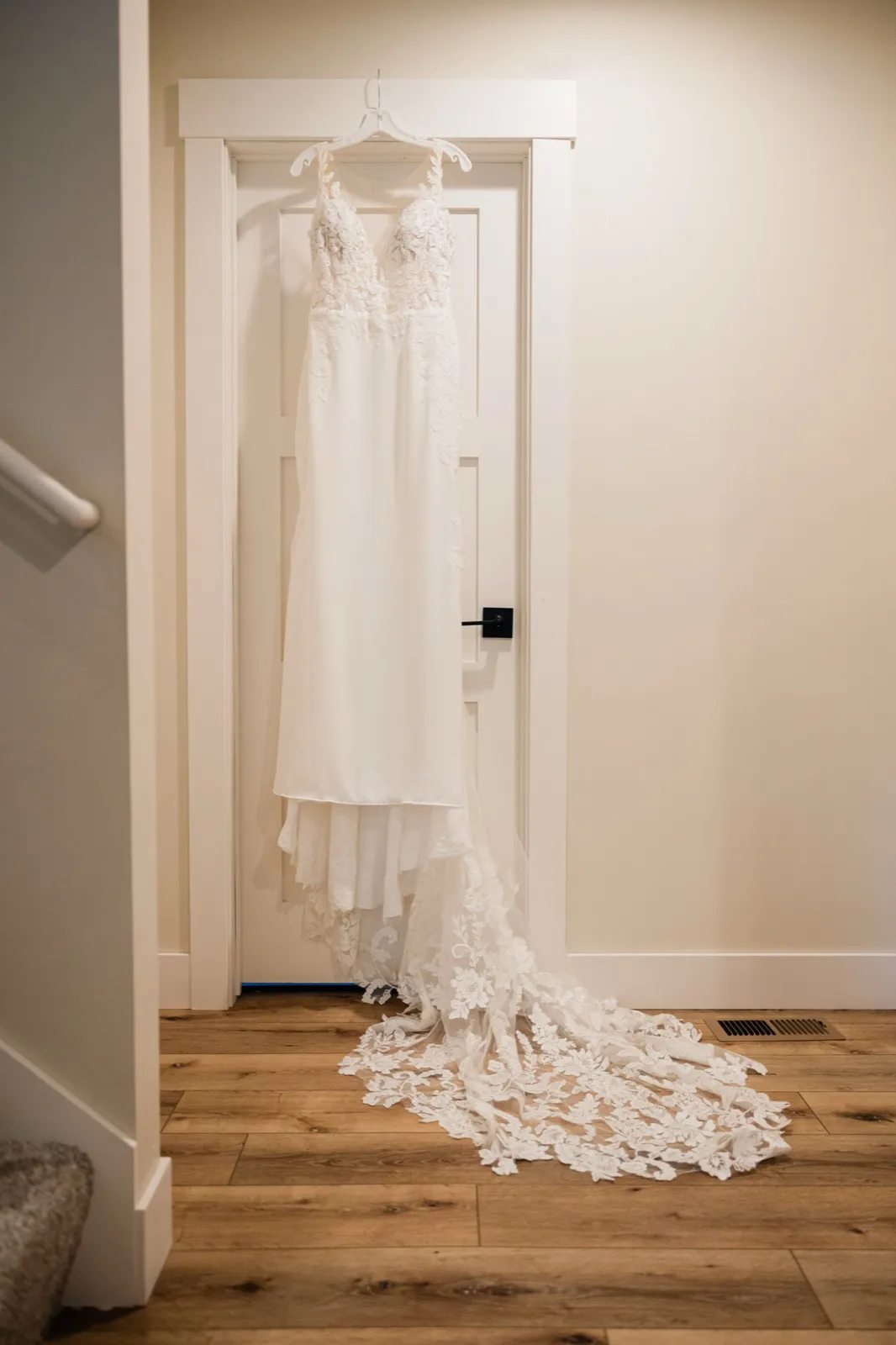 Lauren's white lace wedding dress hangs from a white paneled door, its floral lace train arranged across the wood floor — Tim Larsen Photography, Brainerd Lakes MN