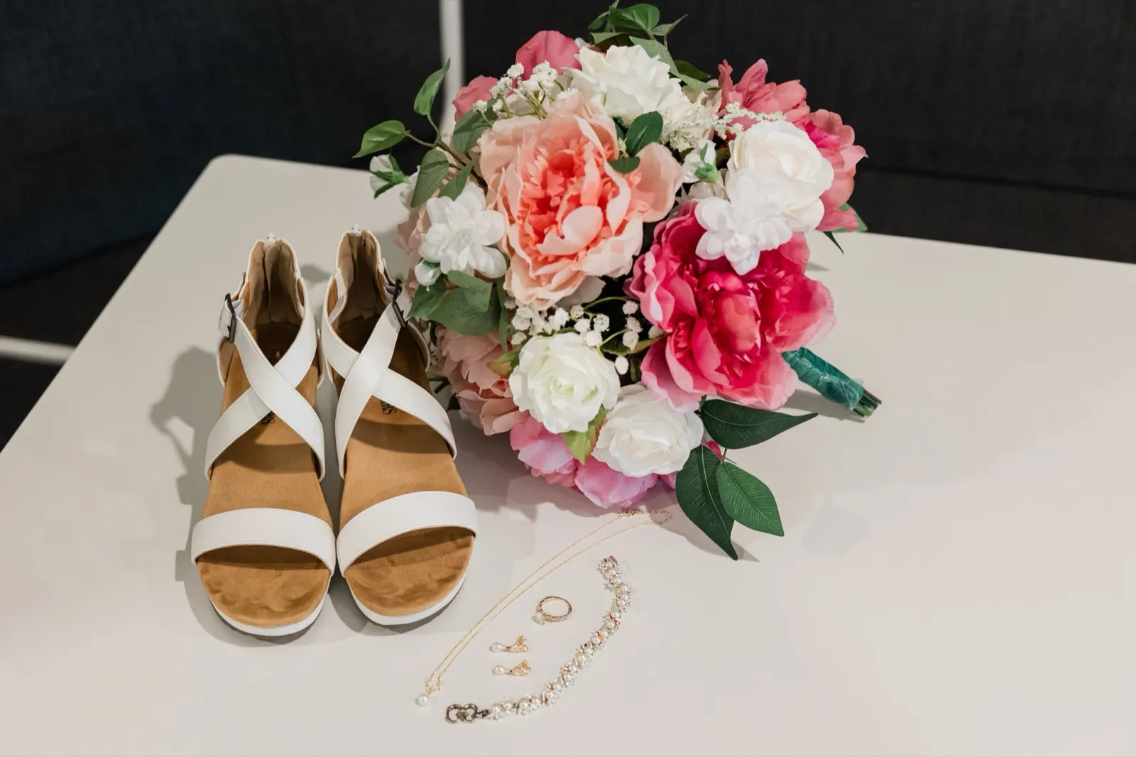 The bride's white sandals, pearl jewelry, and pink-and-white bouquet arranged together on a white table — Tim Larsen Photography, Brainerd Lakes MN