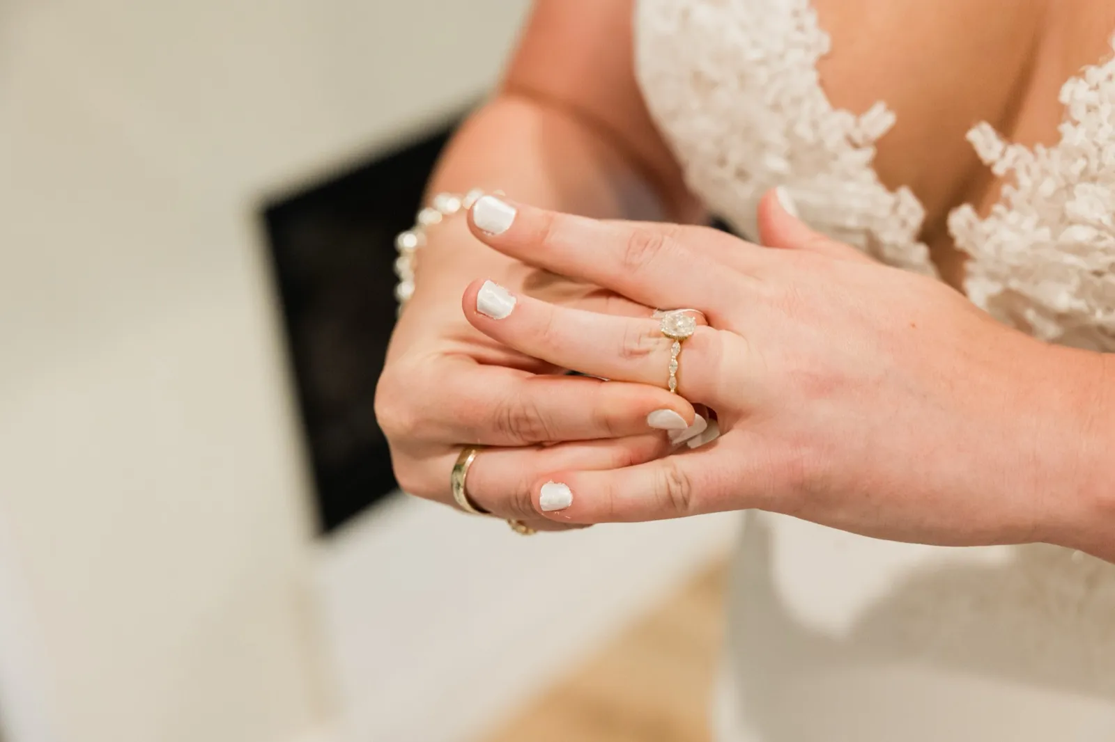 The bride's hands turn an oval diamond engagement ring against the lace bodice of her gown — Tim Larsen Photography, Brainerd Lakes MN
