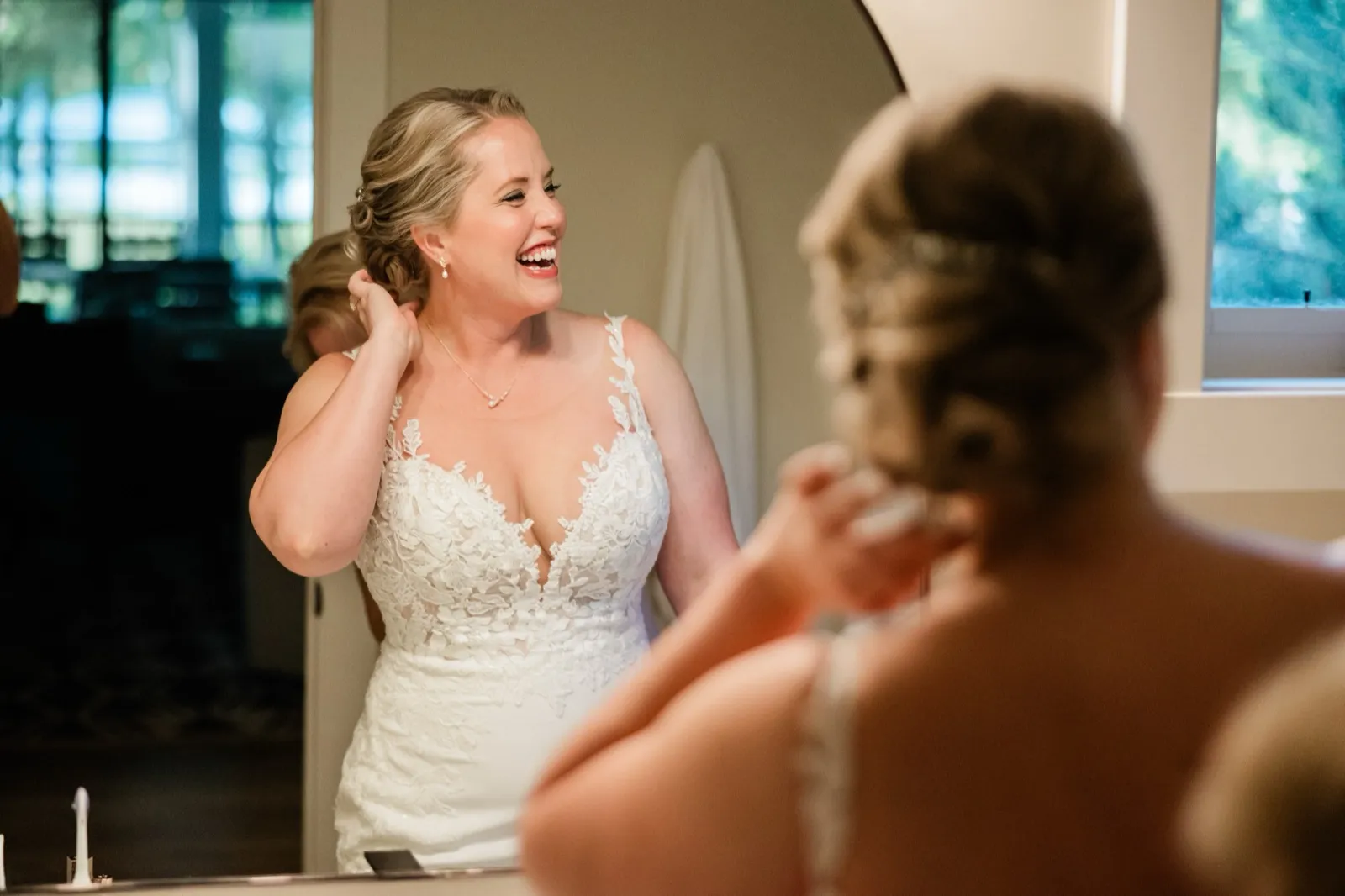 The bride touches her pearl earring, her laughing face reflected in the mirror over her shoulder — Tim Larsen Photography, Brainerd Lakes MN