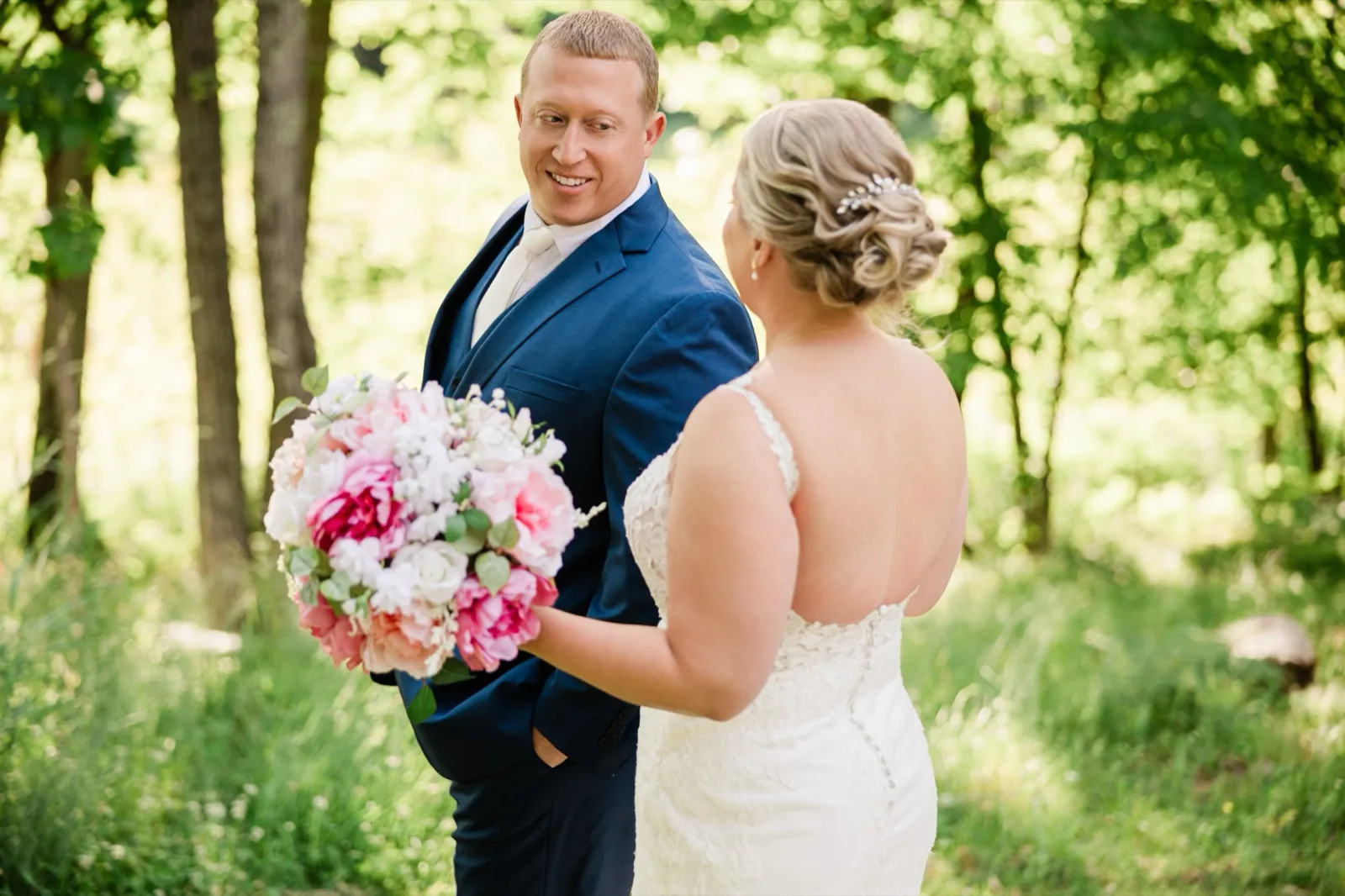 The groom turns and sees the bride for the first time, breaking into a smile in the green woods — Tim Larsen Photography, Brainerd Lakes MN