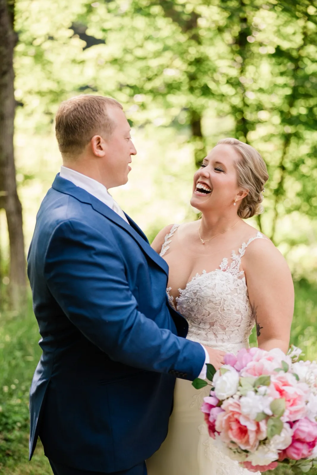 The groom stands in profile as the bride throws her head back laughing in the green woods — Tim Larsen Photography, Brainerd Lakes MN
