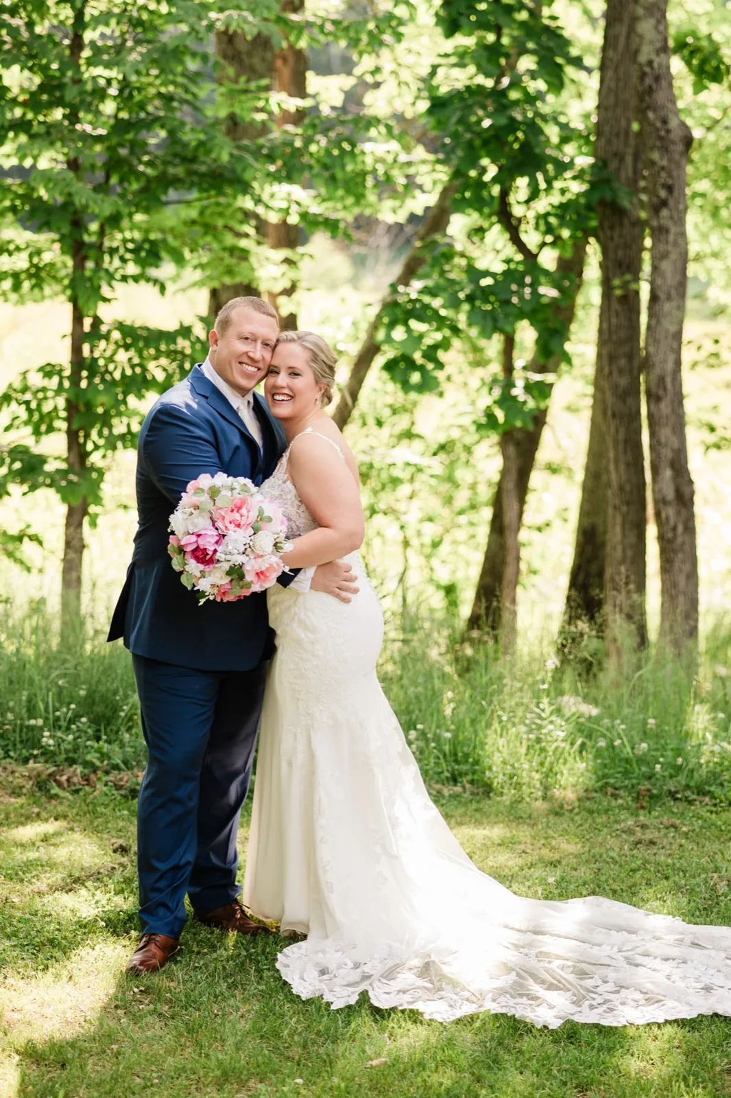 Full-length portrait of the couple embracing, Lauren's lace train spread across the sunlit grass — Tim Larsen Photography, Brainerd Lakes MN