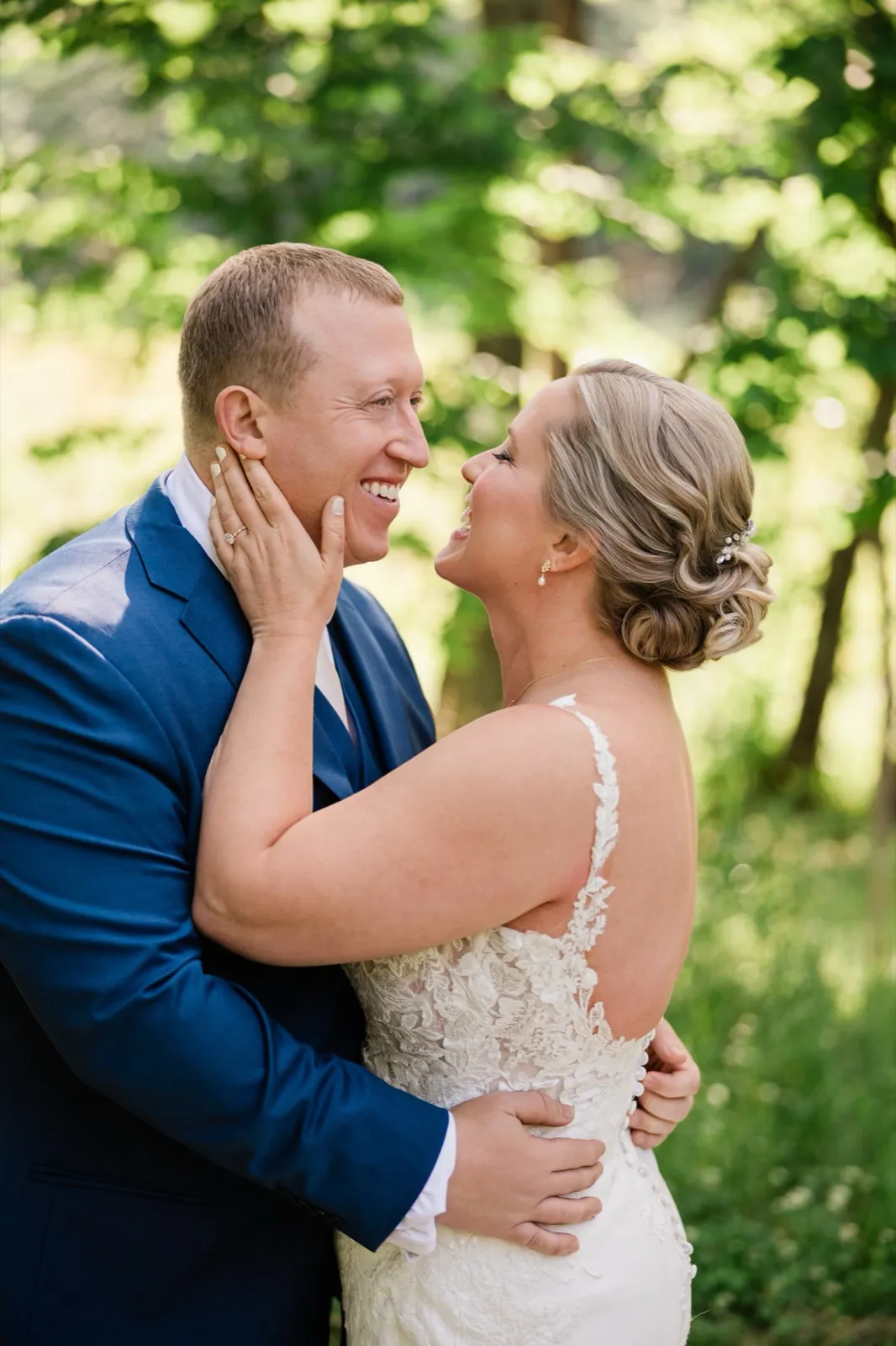 Lauren holds Jeremy's face in both hands as they laugh together in the sunlit woods — Tim Larsen Photography, Brainerd Lakes MN