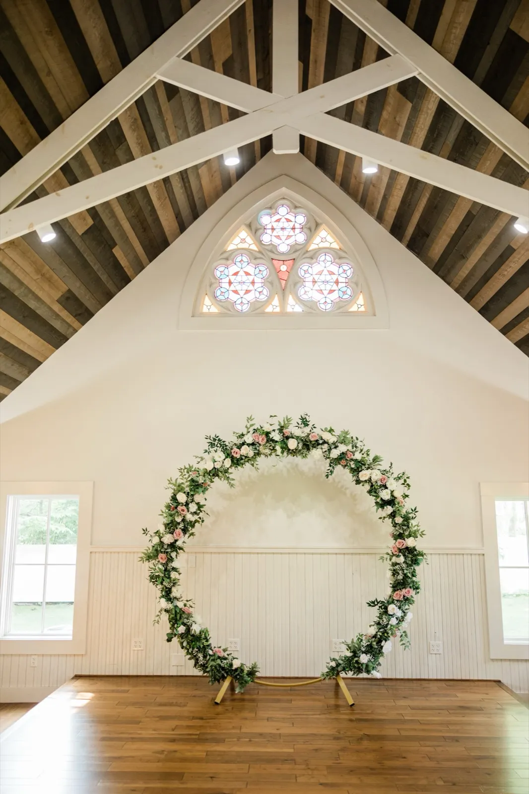 A circular arch of pink and white roses stands on the wooden platform inside The Chapel at Grand View Lodge, stained glass above — Tim Larsen Photography, Brainerd Lakes MN