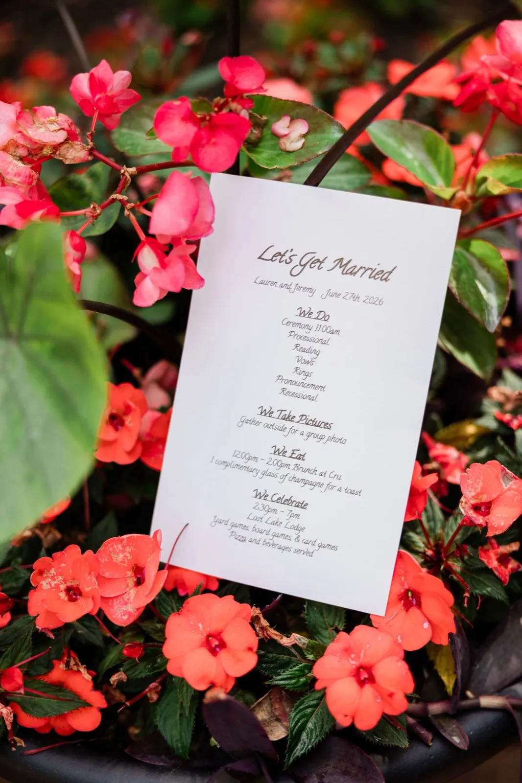 A ceremony program reading 'Let's Get Married — Lauren and Jeremy, June 27th 2026' rests among coral impatiens at Grand View Lodge — Tim Larsen Photography, Brainerd Lakes MN