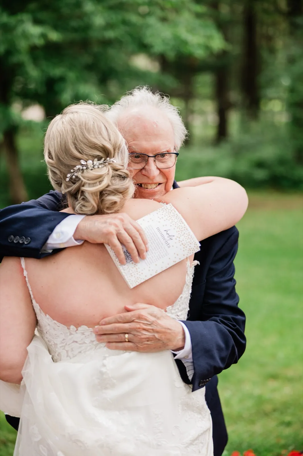 An elderly guest in a navy suit hugs Lauren tightly on the lawn outside the chapel, smiling wide — Tim Larsen Photography, Brainerd Lakes MN