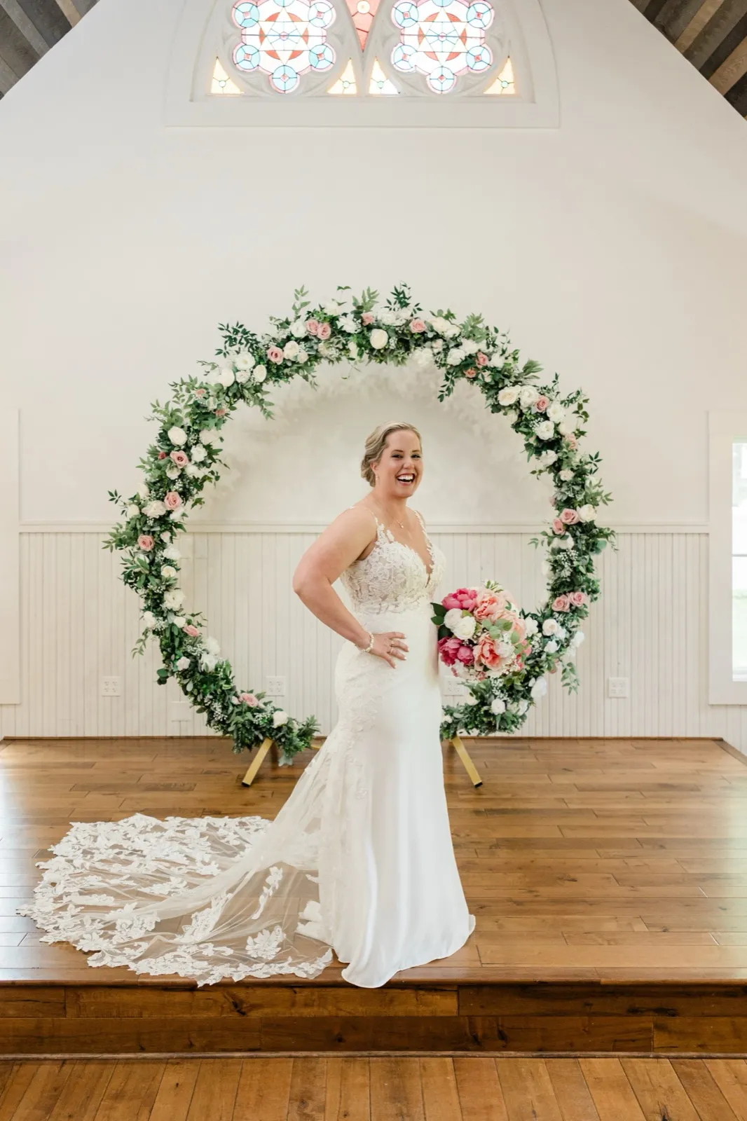 Lauren laughs with a hand on her hip inside the circular rose arch at The Chapel at Grand View Lodge, her train fanned across the floor — Tim Larsen Photography, Brainerd Lakes MN