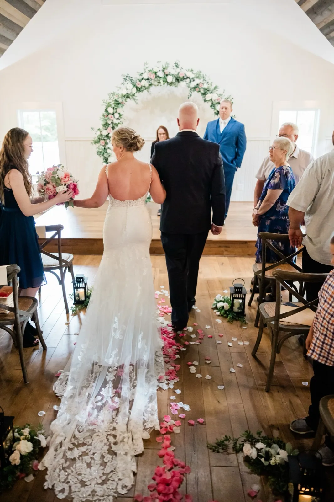 Seen from behind, the bride and her father approach the circular floral arch where Jeremy waits — Tim Larsen Photography, Brainerd Lakes MN