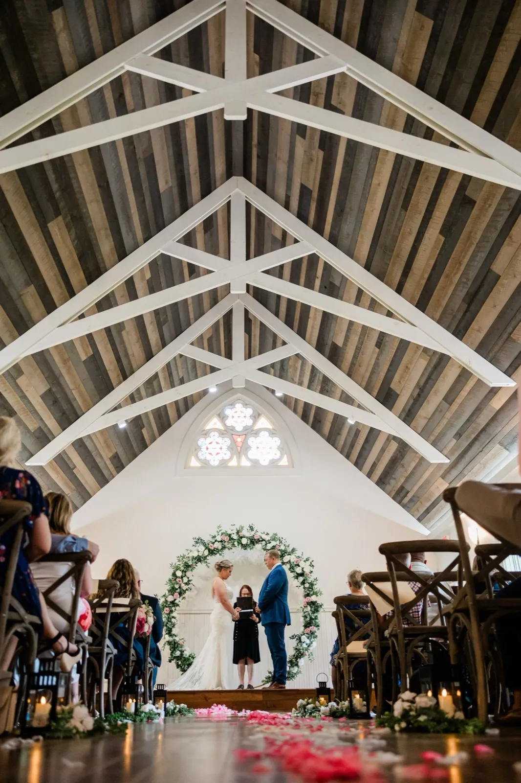 A low wide view of the couple at the floral arch beneath the white trusses and stained glass of the Grand View Lodge chapel — Tim Larsen Photography, Brainerd Lakes MN